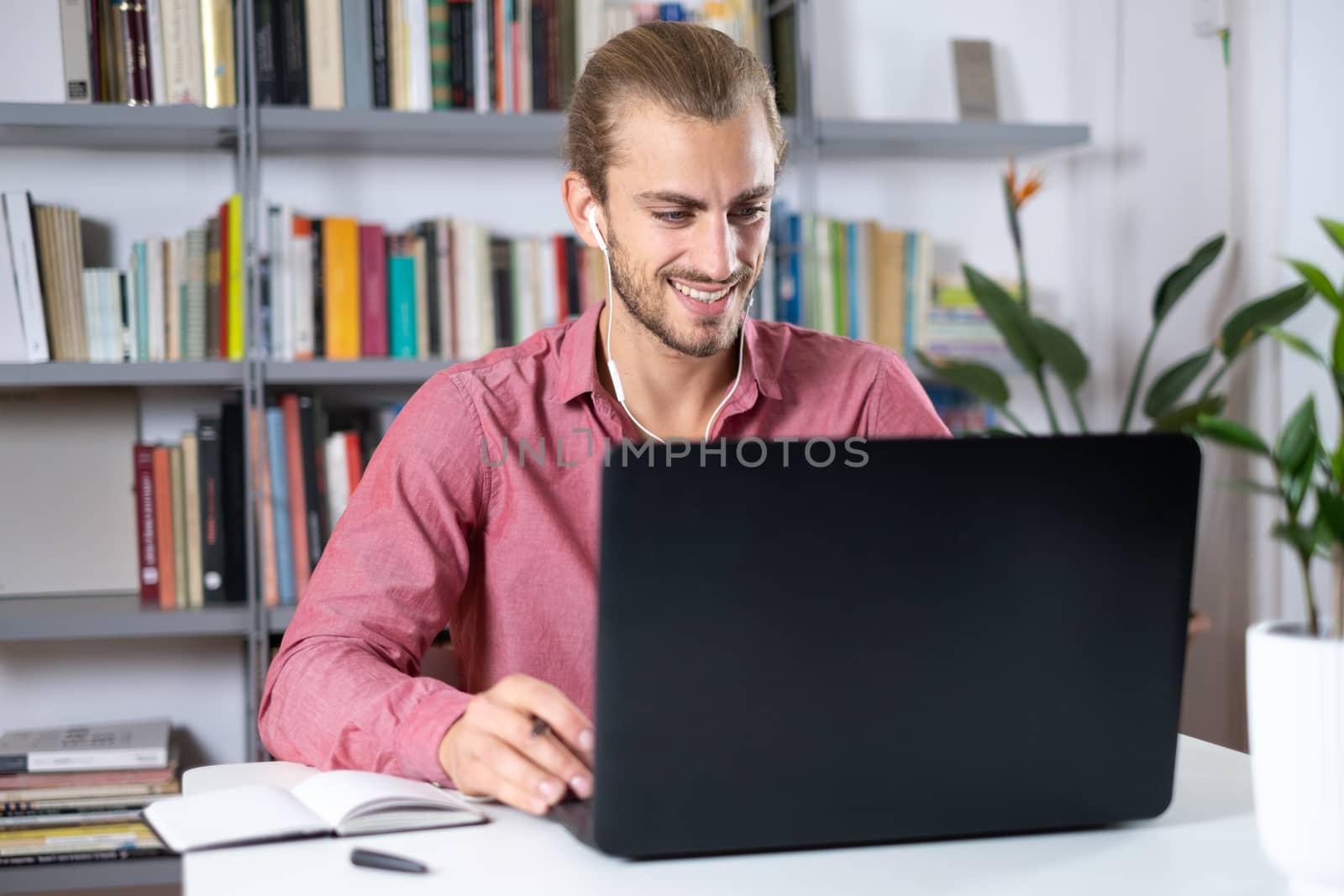 Attractive young man sitting at the table at home working with a laptop on a meeting and feeling happy