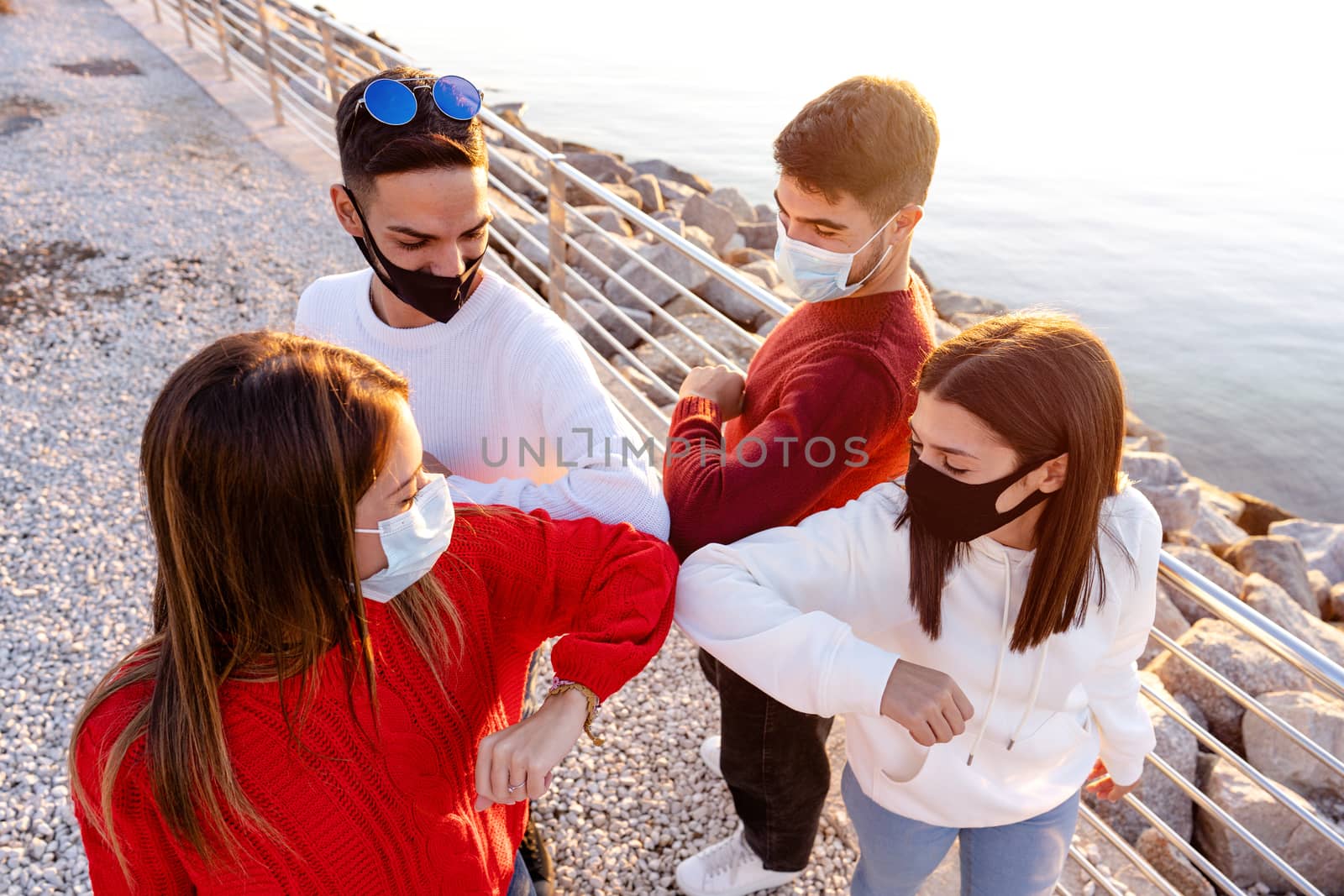 Top view of a group of young friends wearing protective face masks greeting bumping elbows outdoor Near the sea rocks in a vacation place in Sardinia - New normal contacts with social distancing
