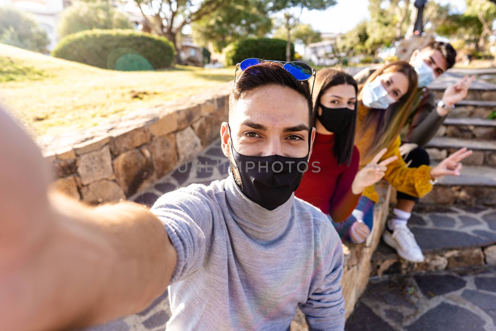 Outdoor group portrait of happy young people with medical mask - Millennial man take a selfie with his friends lined up behind him - New normal outdoor activity with Coronavirus pandemic by robbyfontanesi