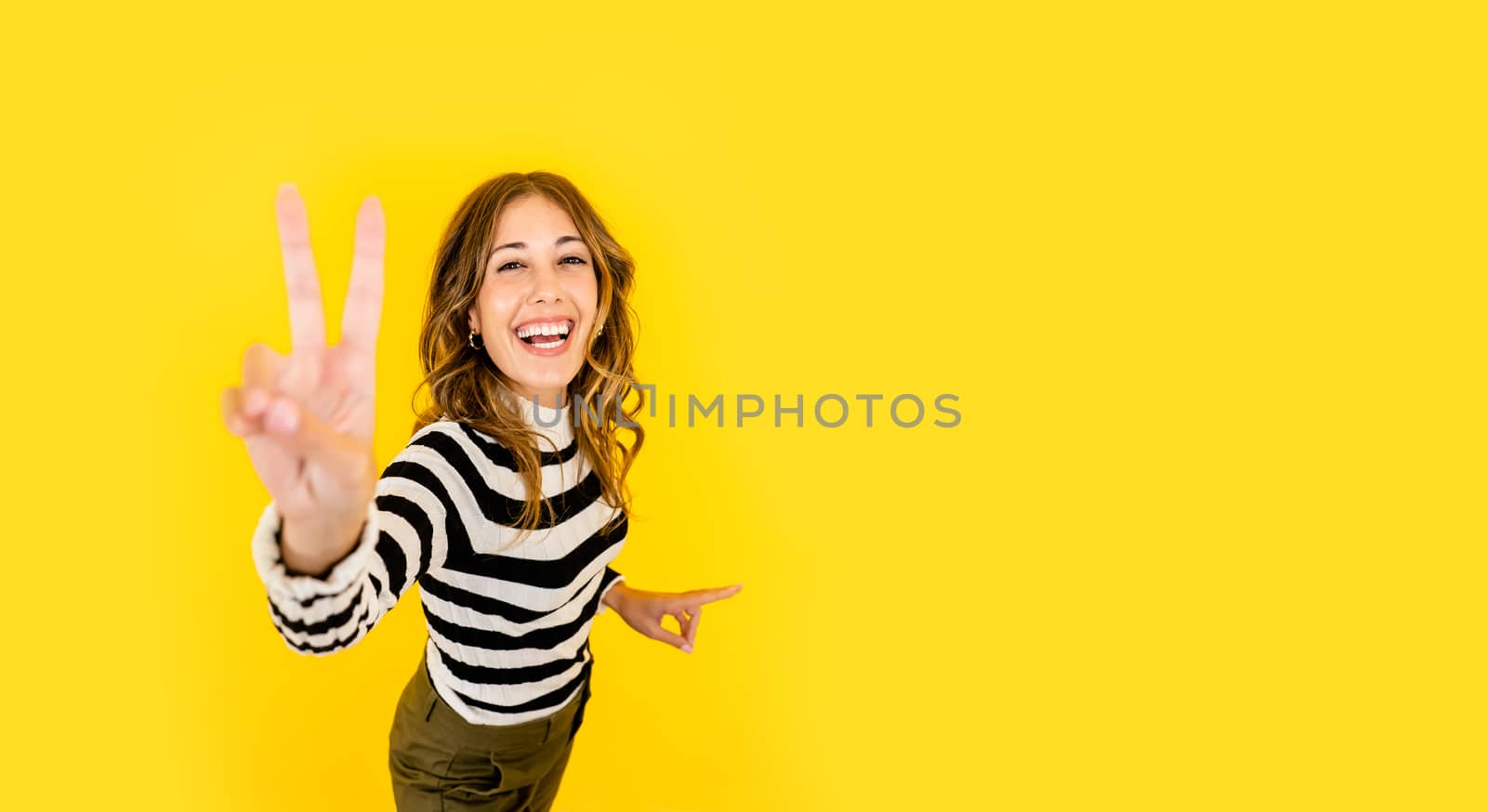 Cute happy young woman with black and white striped shirt does the victory sign looking and smiling at the camera - Studio shot of female single millennial in positive and confident pose by robbyfontanesi
