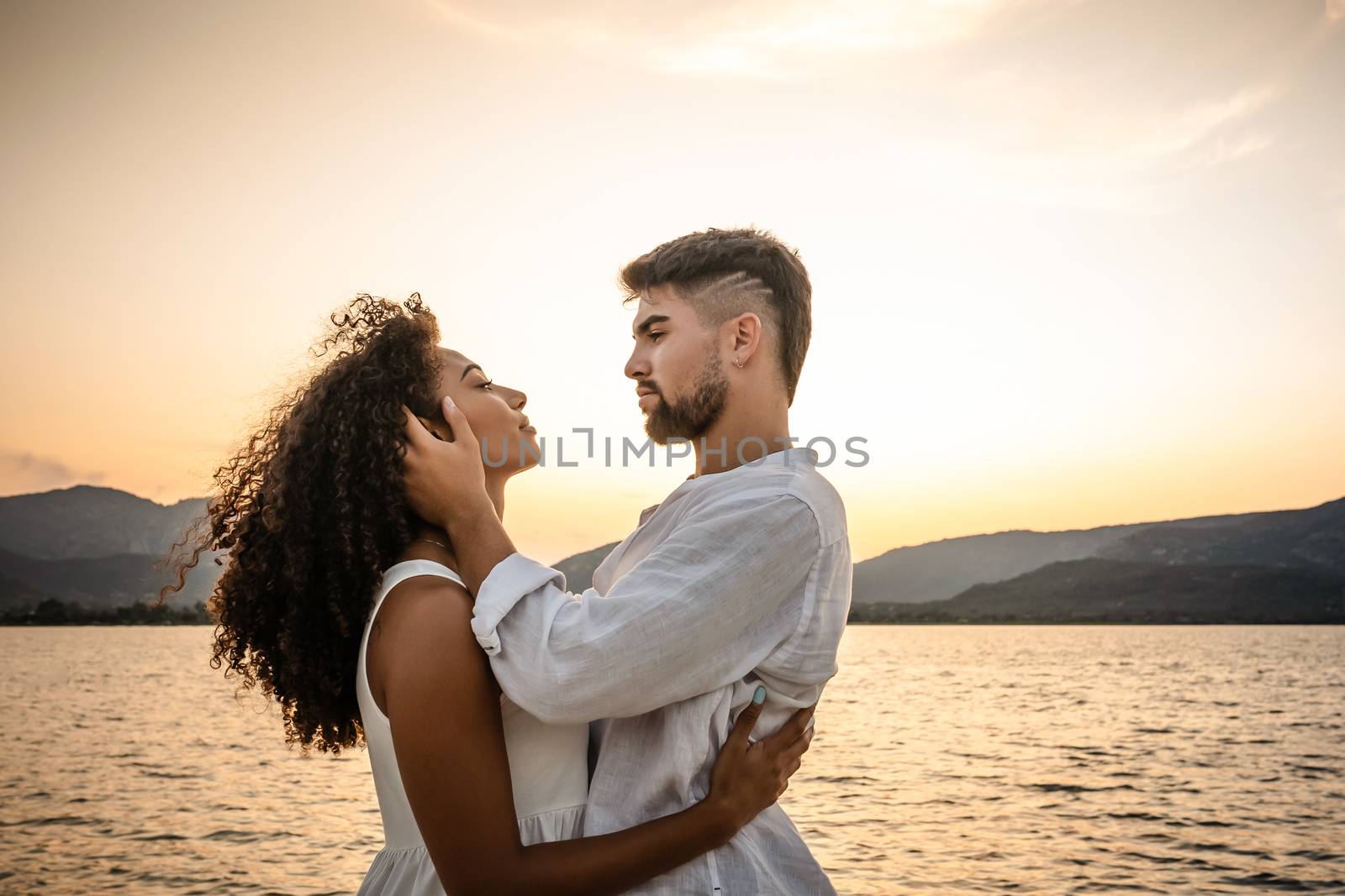 Attractive mixed race lovers couple in romantic pose in sunset backlight - Strong serious bearded young handsome man holding face of her black Hispanic girlfriend looking in her eyes with passion