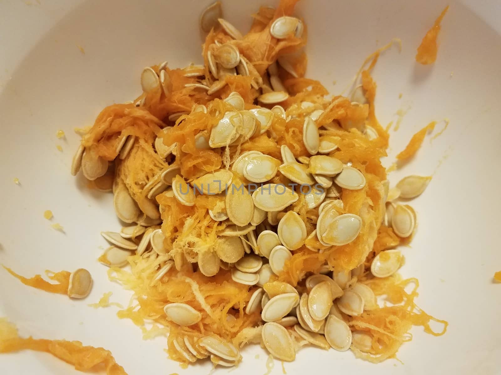 pumpkin seeds and orange pulp in white container