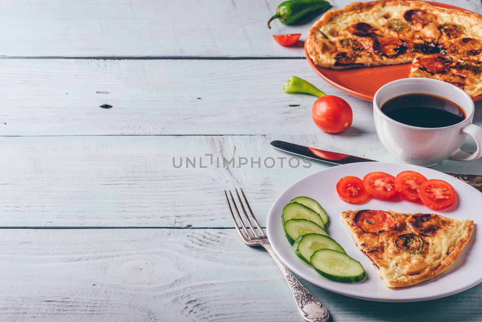 Breakfast frittata with chorizo, tomatoes and chili peppers on plate and cup of coffee over light wooden background. Healthy eating food concept.