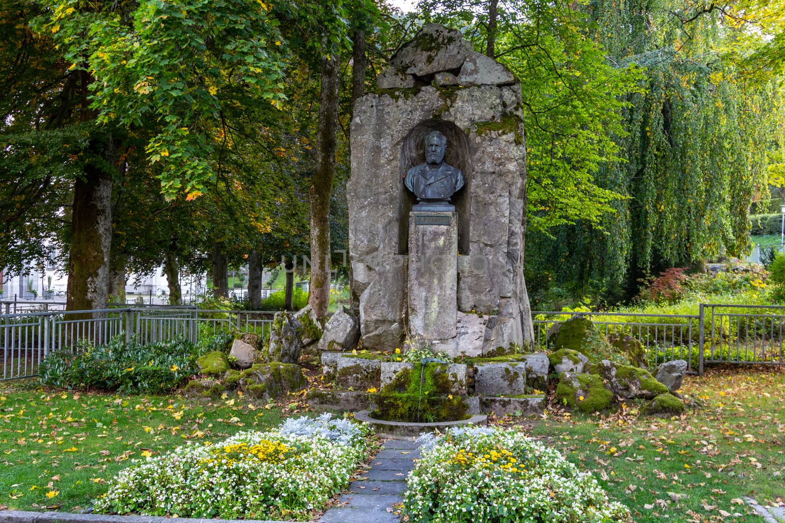 Krafft monument in St. Blasien Black Forest, Germany, trees with multi colored leaves, white and yellow flowers in the foreground
