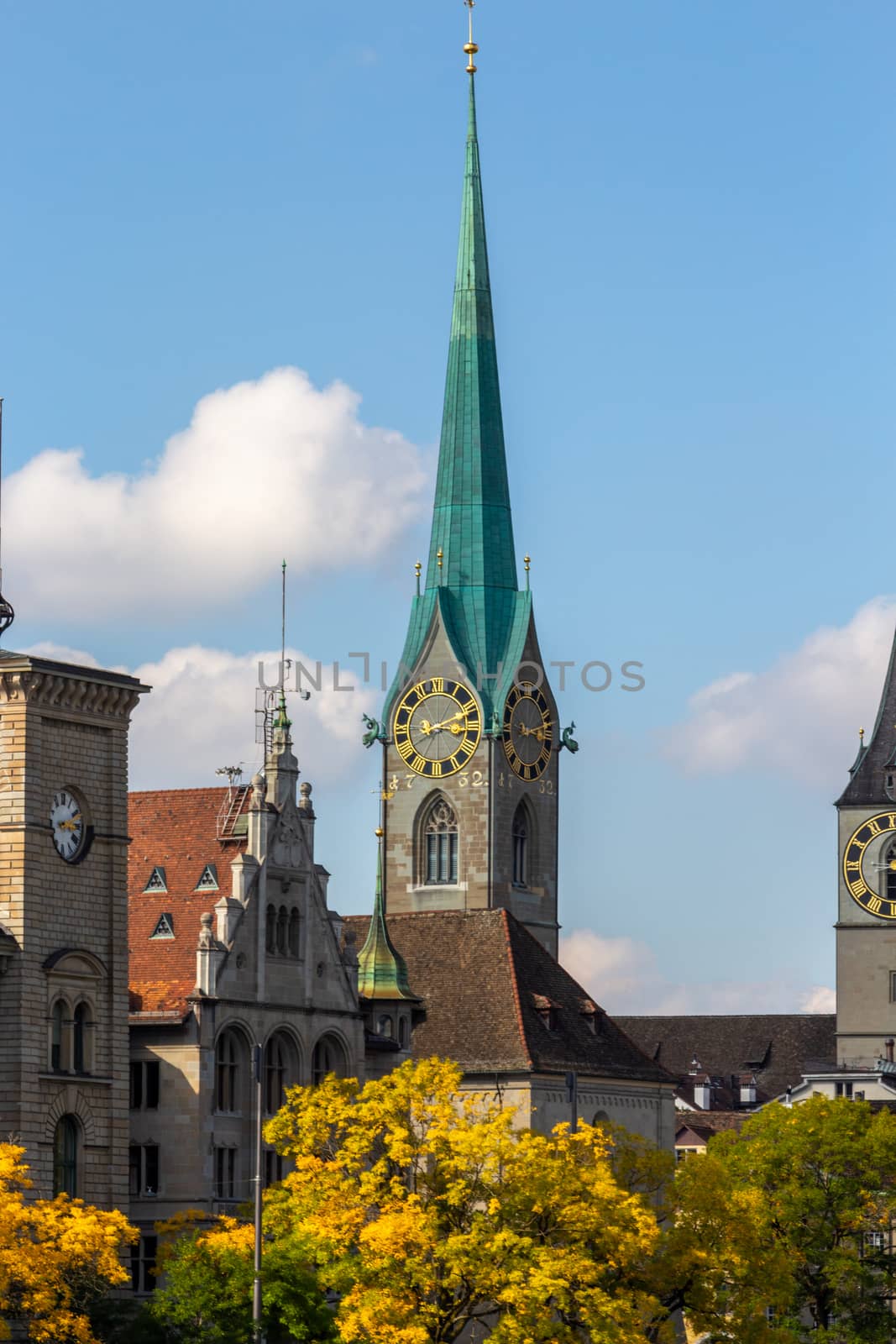 The tower of Fraumuenster church in Zurich, Switzerland in autumn, with multi colored trees in the foreground