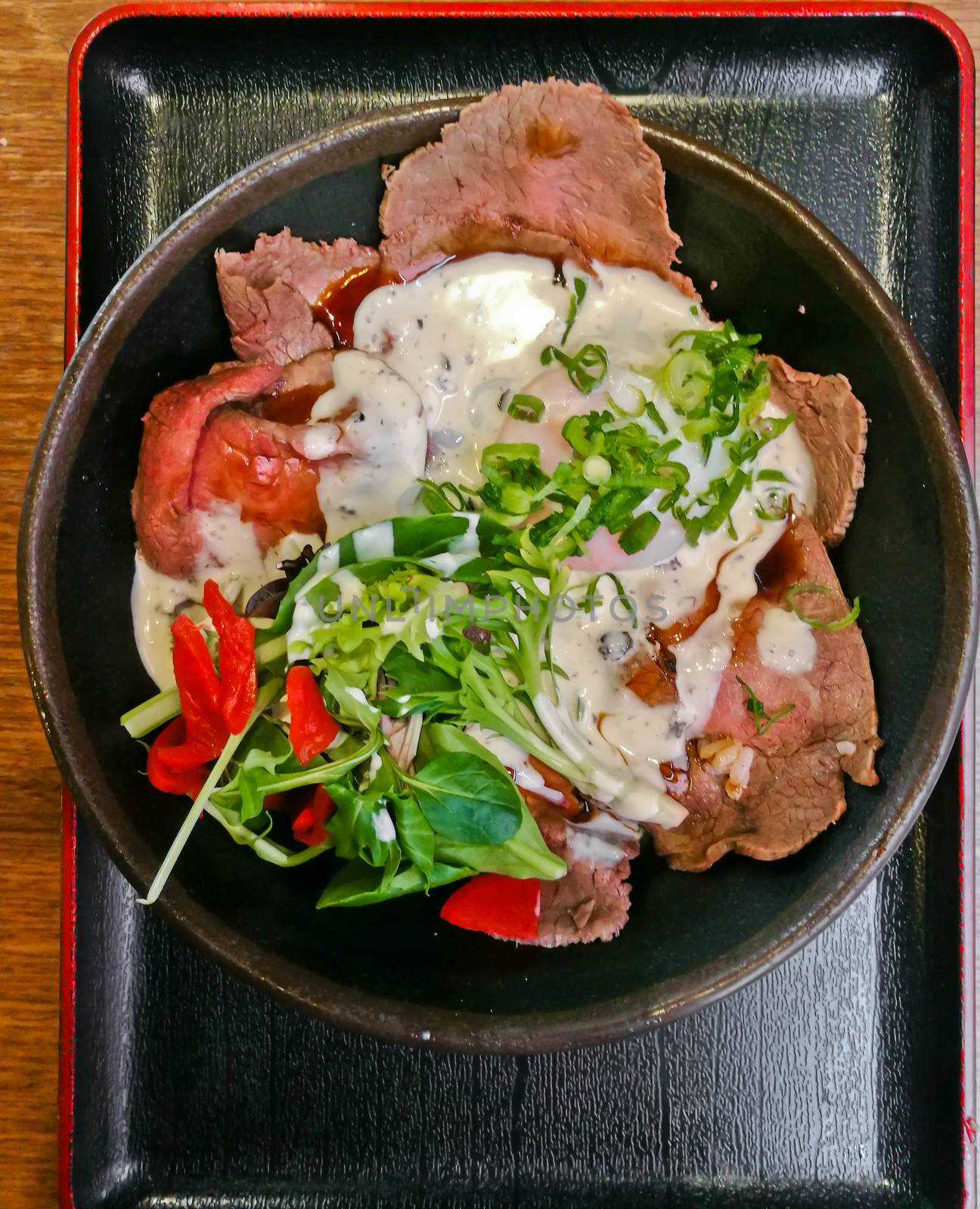 Premium Japanese beef Wagyu thin sliced topping with white Italian dressing sauce and salad in a bowl