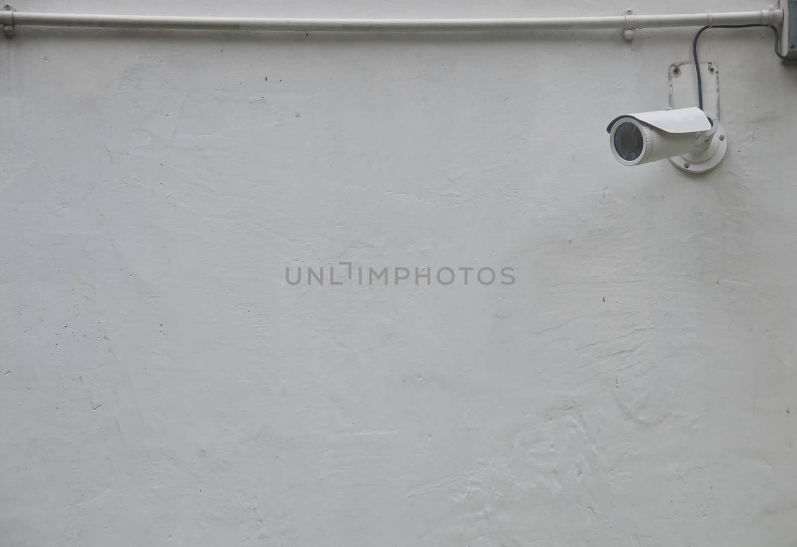 White CCTV security camera with wired data line attached on a white concrete wall