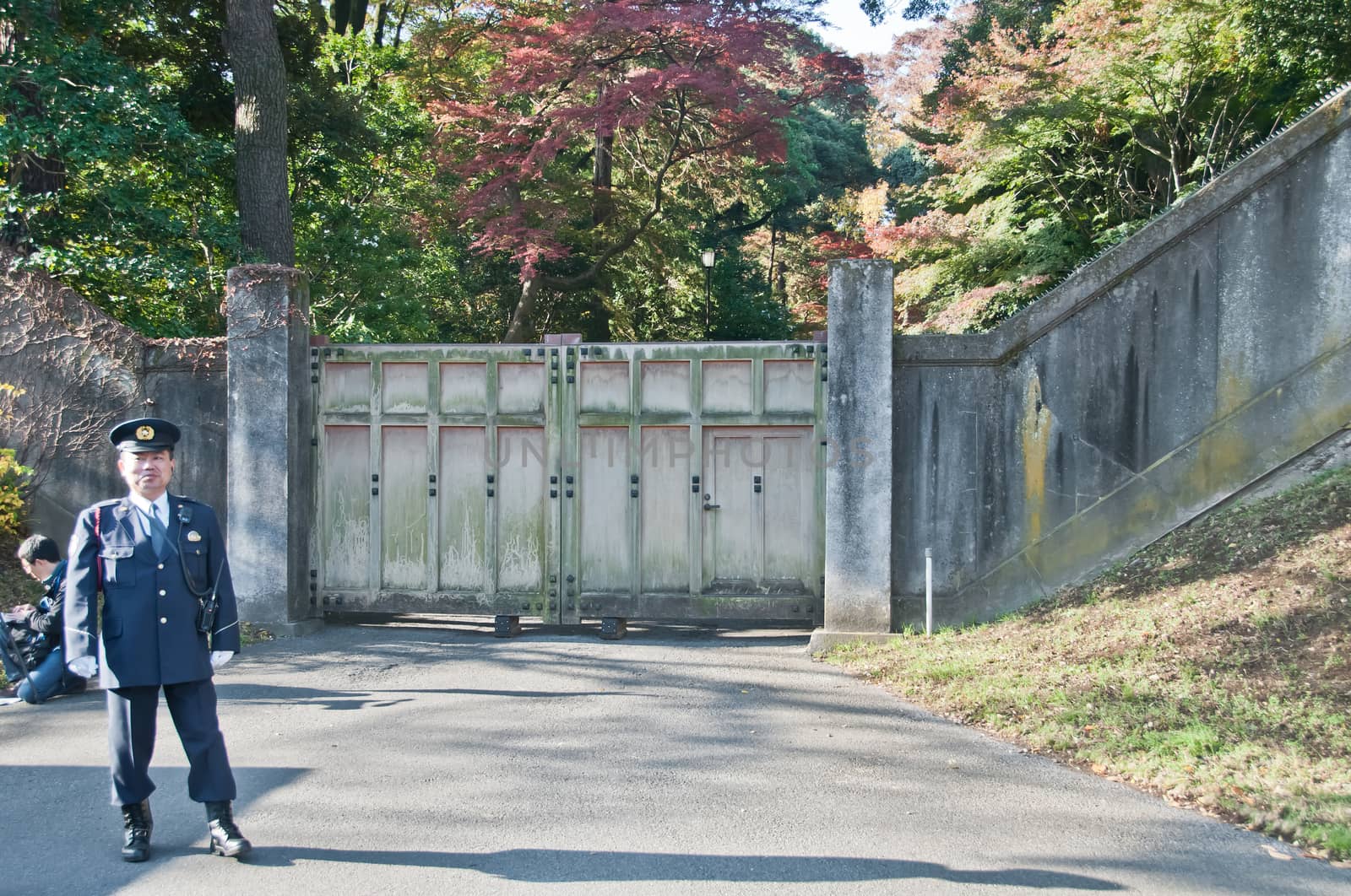 TOKYO, JAPAN - DECEMBER 1, 2018: A Japanese police guard stands in front of internal park gate with a man sits inside the Japanese Royal Imperial Palace.