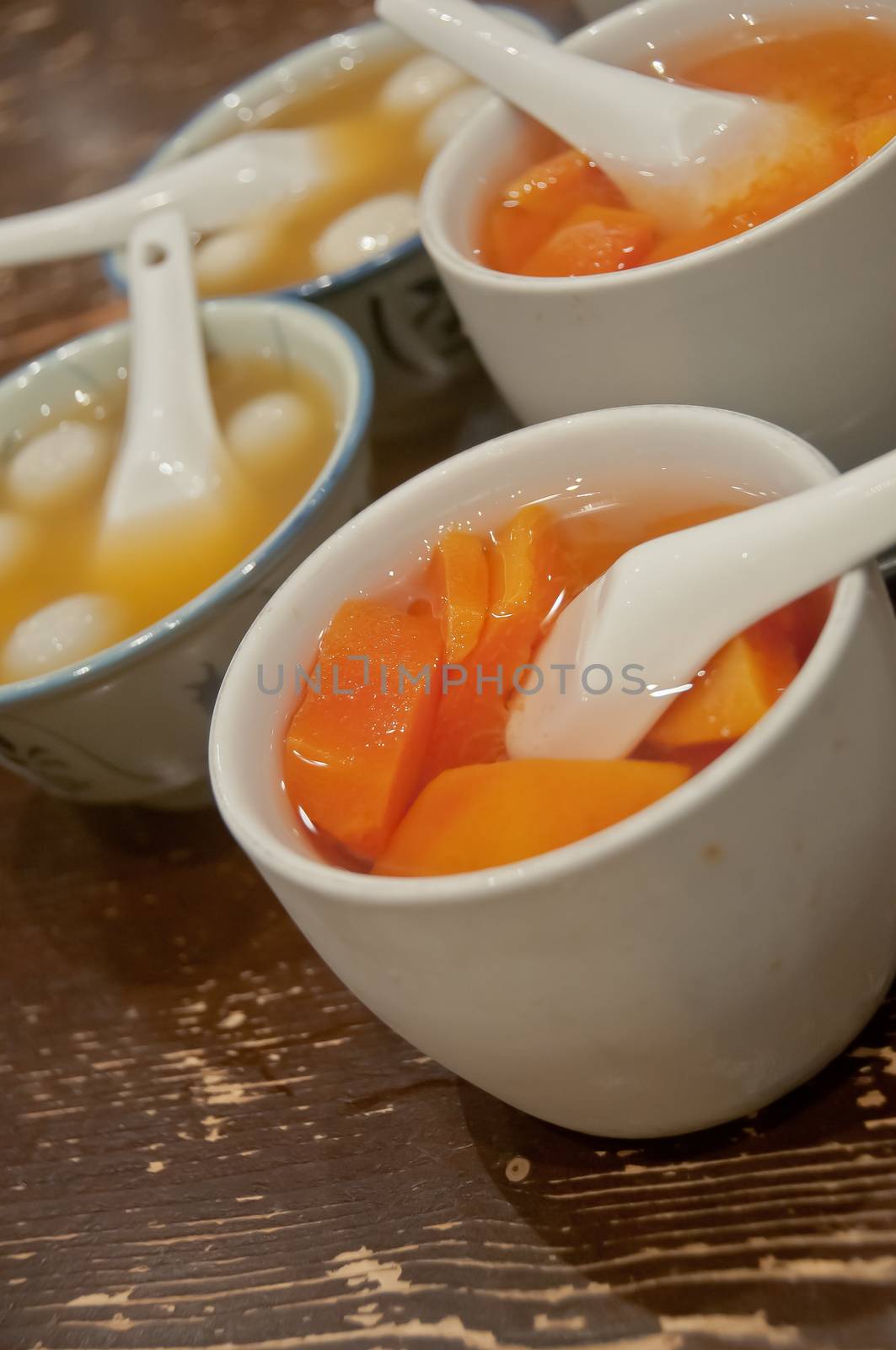 Many bowls of famous hot and cold sweet dessert soup in a round table with her friend in Hong Kong restaurant cafe. There are black sesame soft silky balls and sweet papaya soup