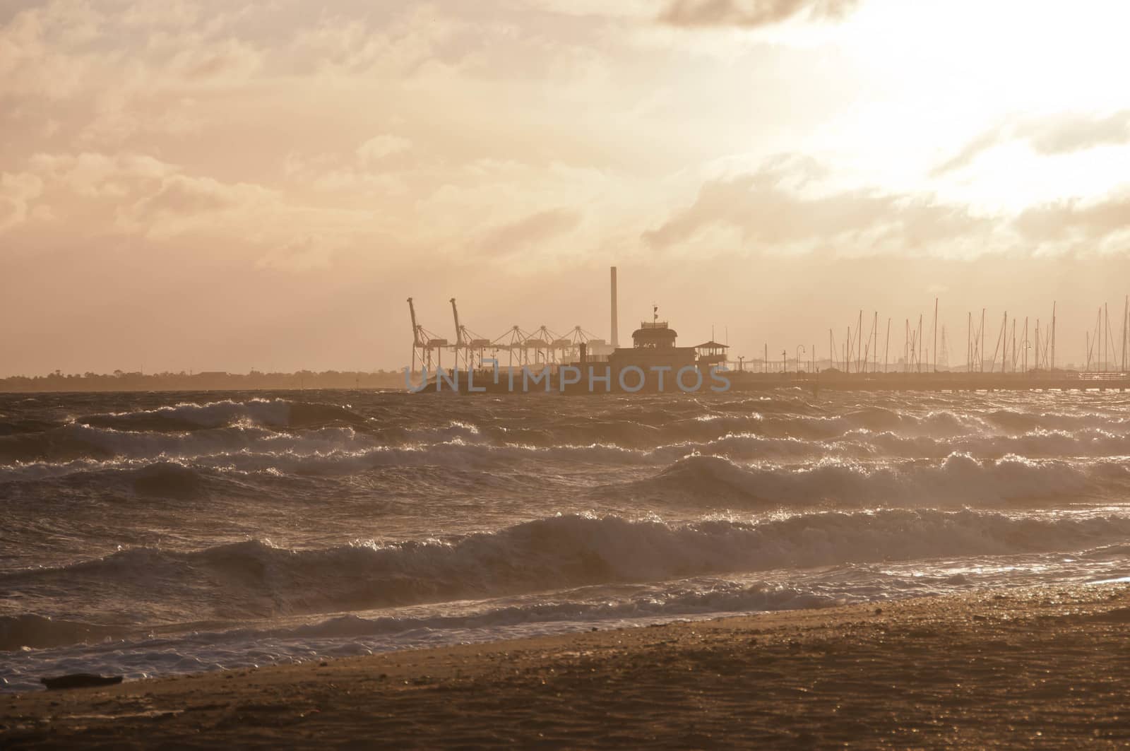 MELBOURNE, AUSTRALIA - JULY 29, 2018: Dramatic golden light ray from the sky in the afternoon with St Kilda pier and windy ocean in Melbourne bay and high tide wave. Nobody is in the photo.