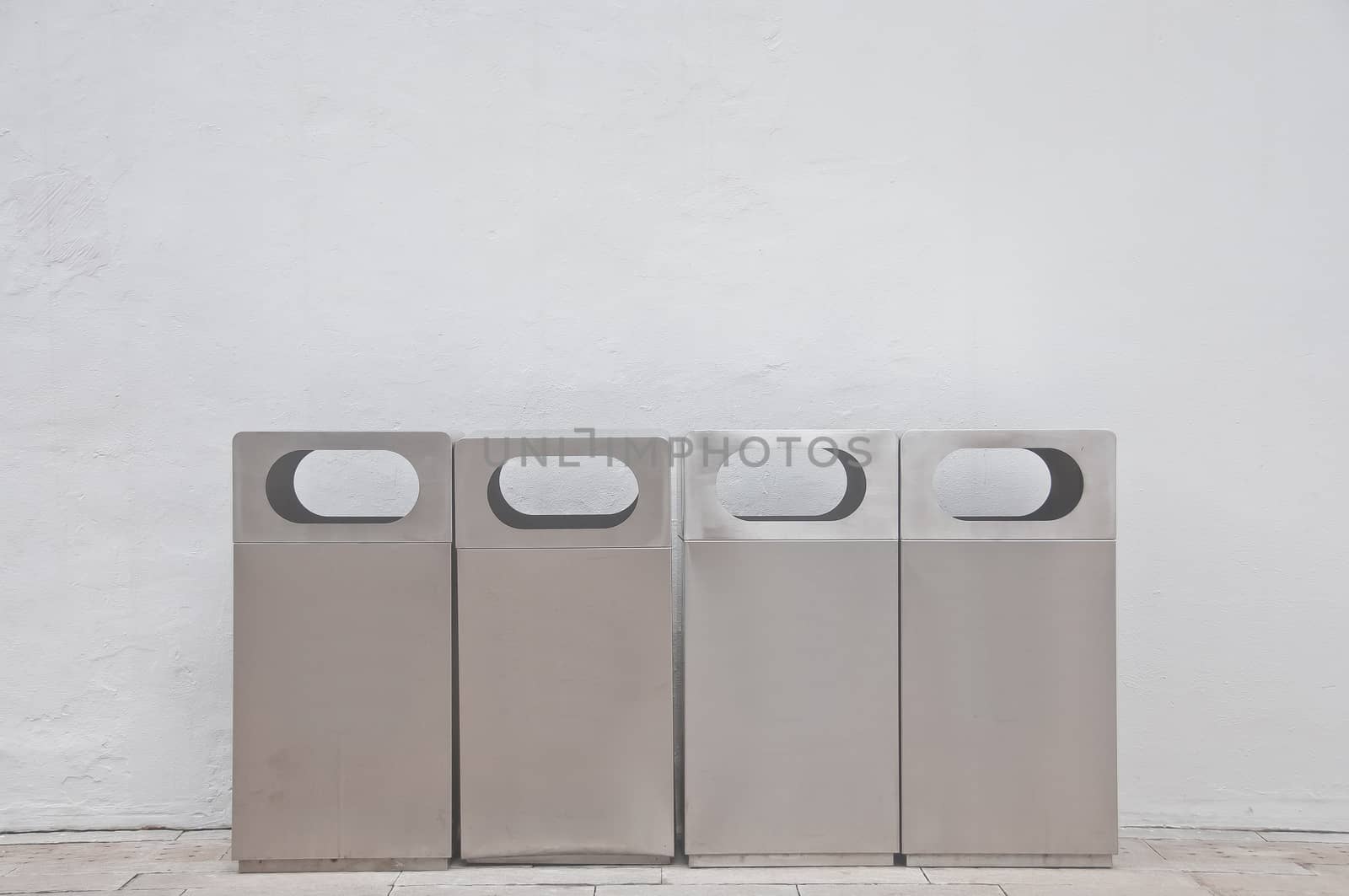 Four of different types of grey metal bins lays in front of white building wall