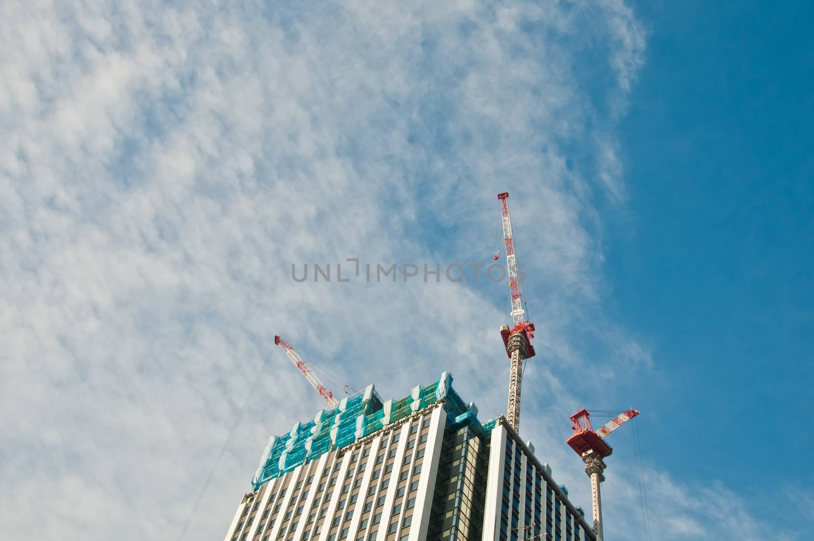 Underconstruction building in progress with many construction cranes and bright sunny blue sky with cloud