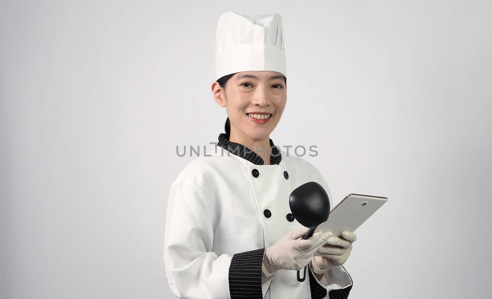 Asian woman chef holding smartphone or digital tablet and received food order from online shop or merchant application. she smiling in chef uniform and standing in studio with white color background.