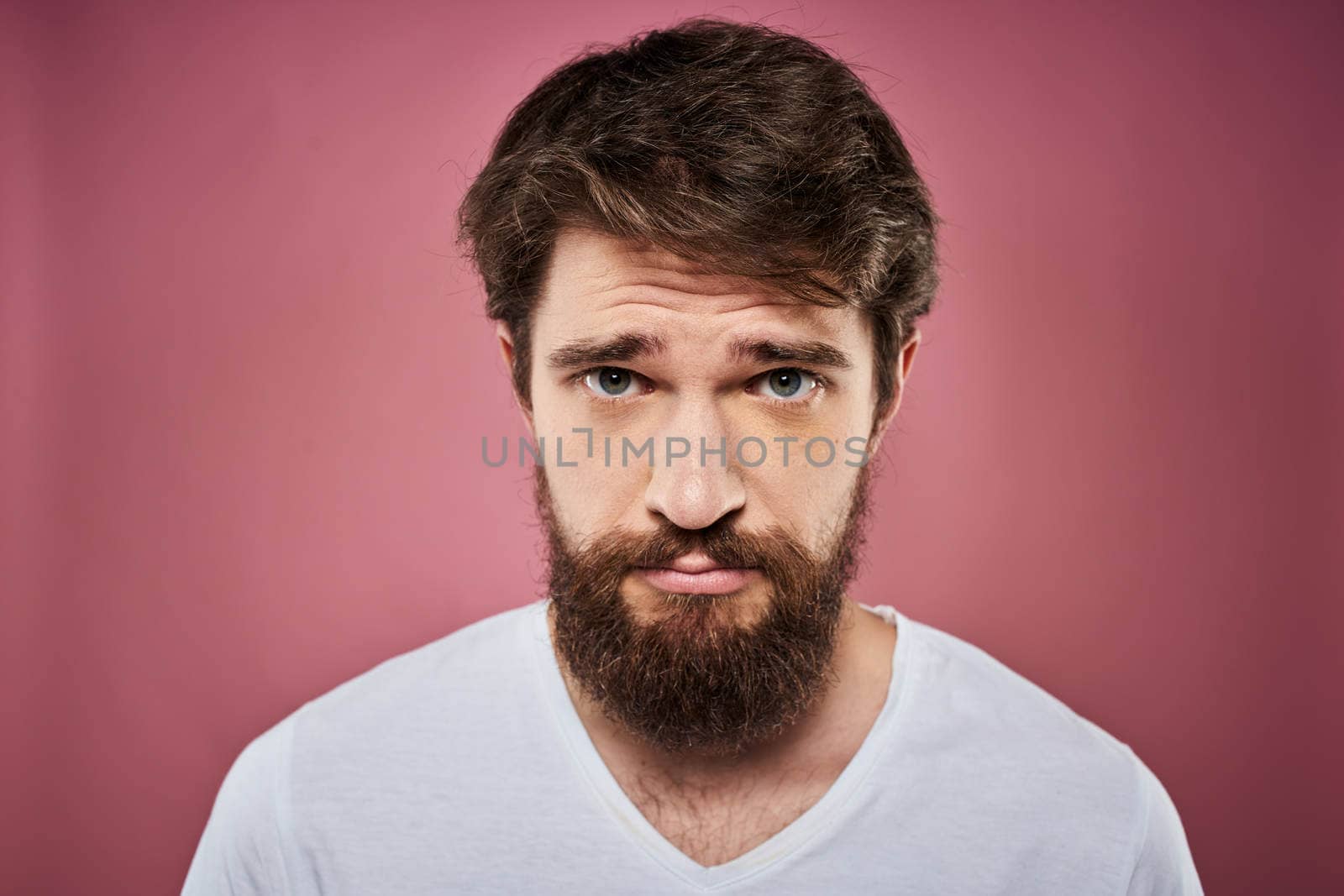 Emotional bearded man in white T-shirt discontent pink background. High quality photo