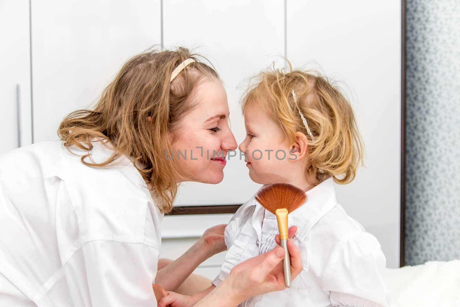 Portrait of woman doing makeup to her daughter in the bedroom on the bed.