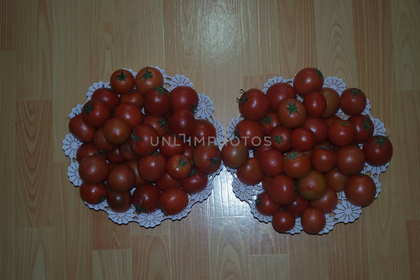 Close-up view of red tomatoes in white basket on a wooden floor in market by Photochowk