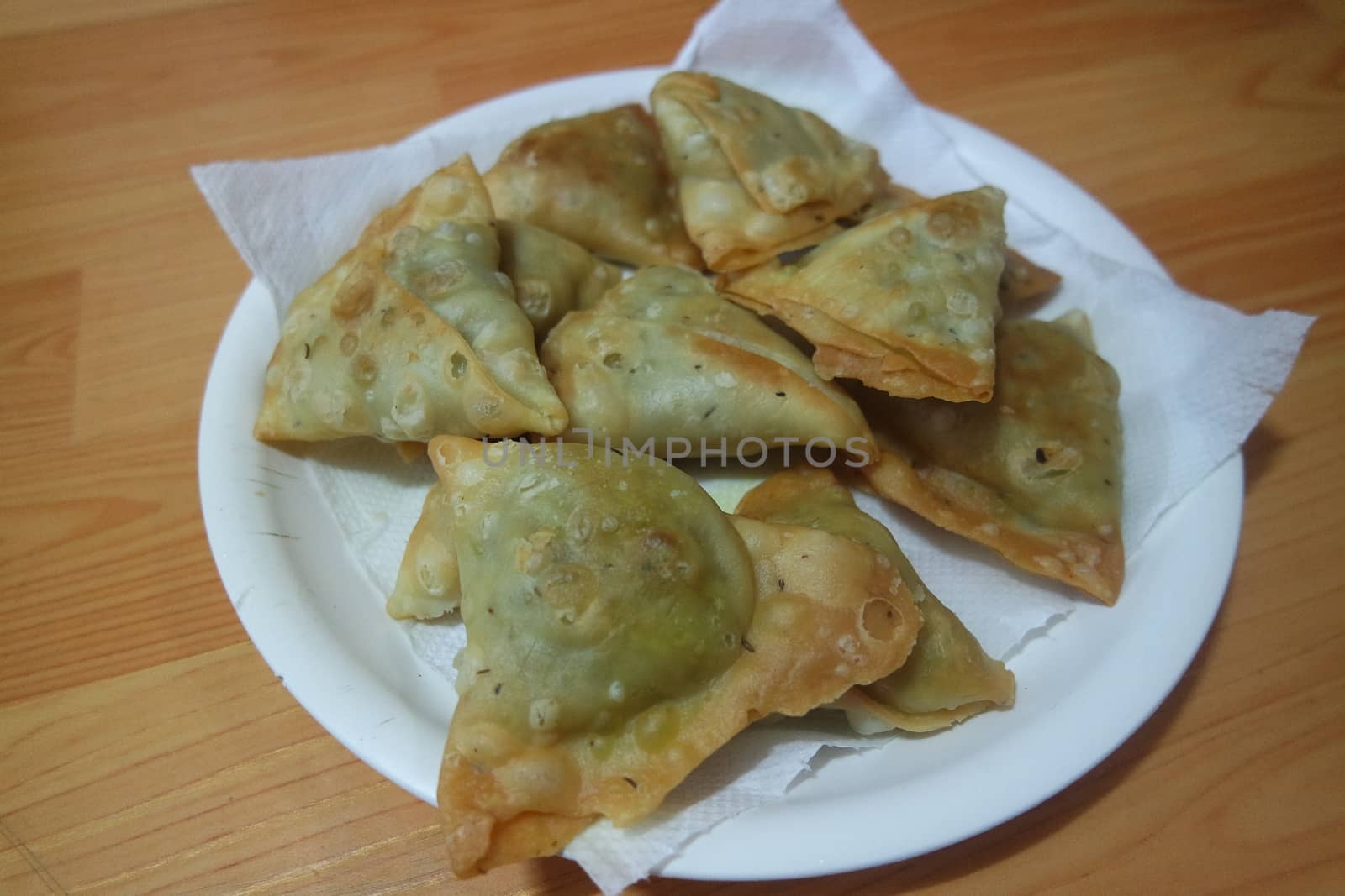 Closeup of delicious home made spicy and crunchy samosa pastries placed in a white ceramic plate on wooden floor