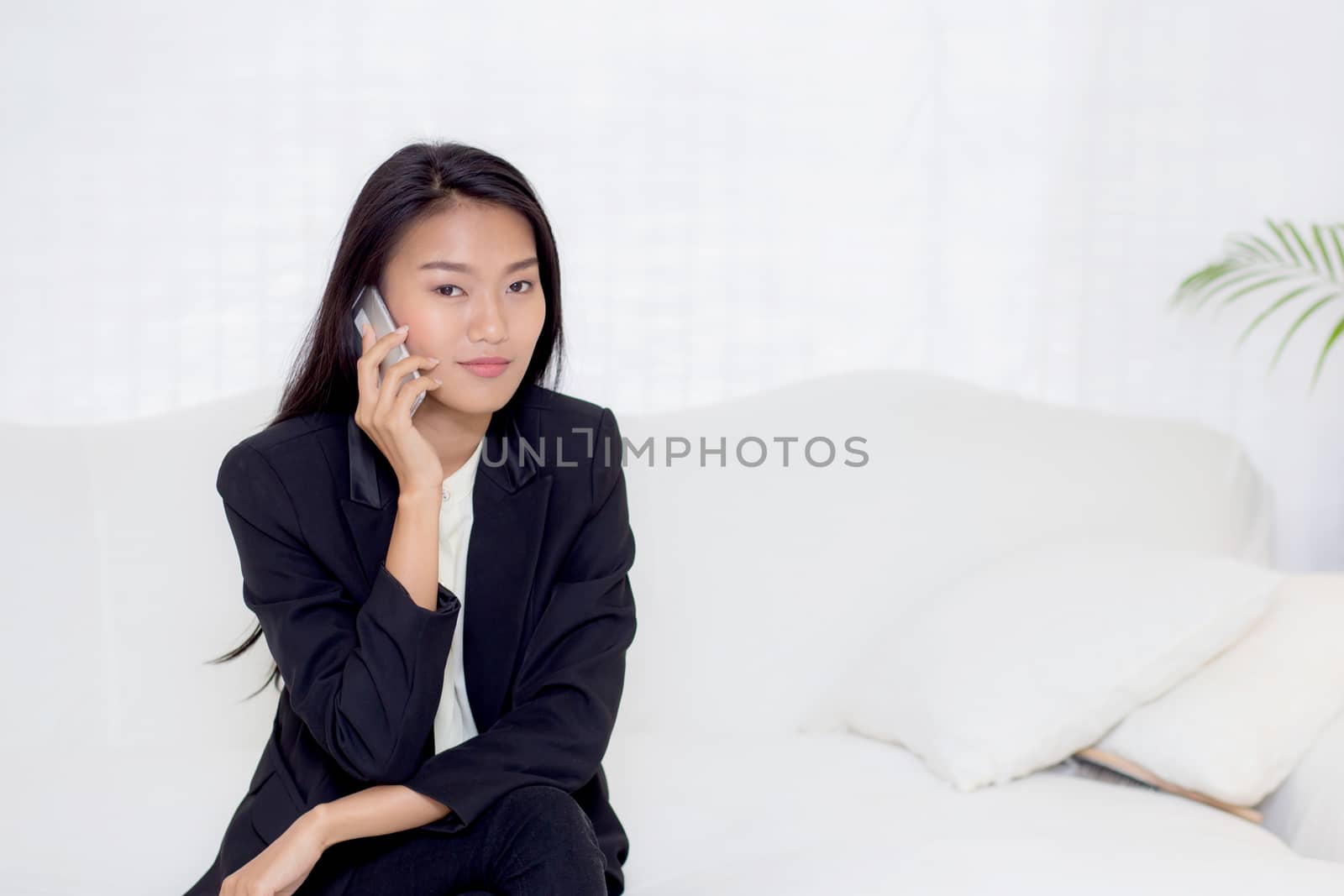 Beautiful young asian woman talking phone and smile in the living room, businesswoman sitting on sofa,businesswoman calling telephone, communication concept.