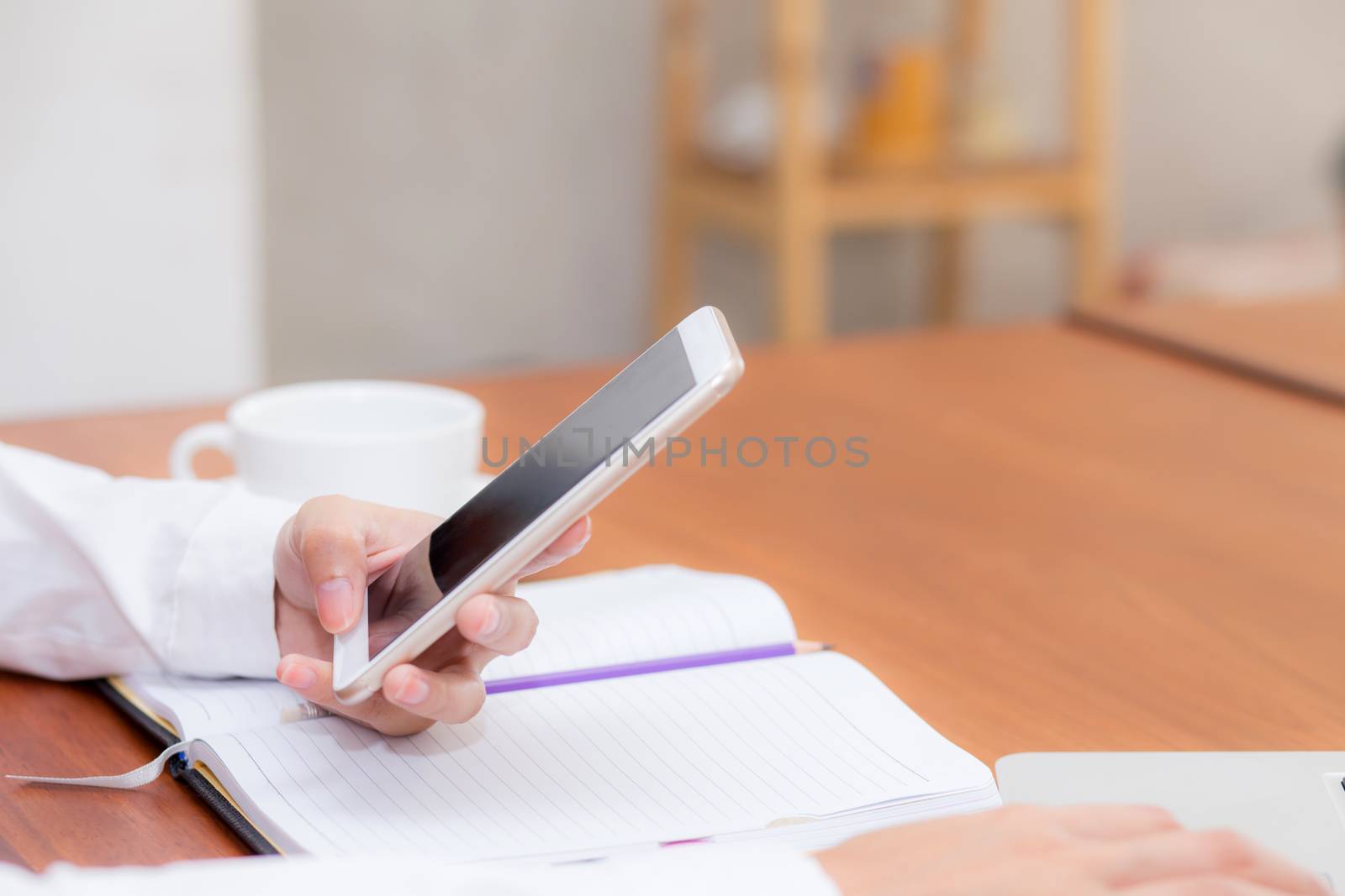 Closeup woman hand with mobile smart phone and notebook at coffee shop, girl working at cafe, communication business concept.
