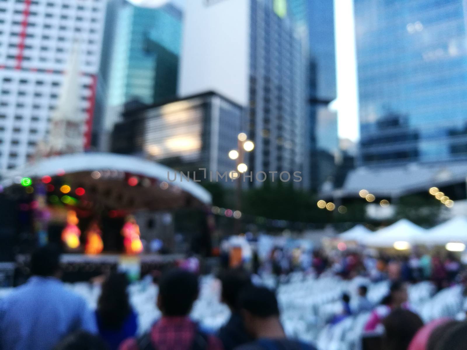 Defocused scene of crowd of people attending public concert celebrating New Year festival in city in Evening