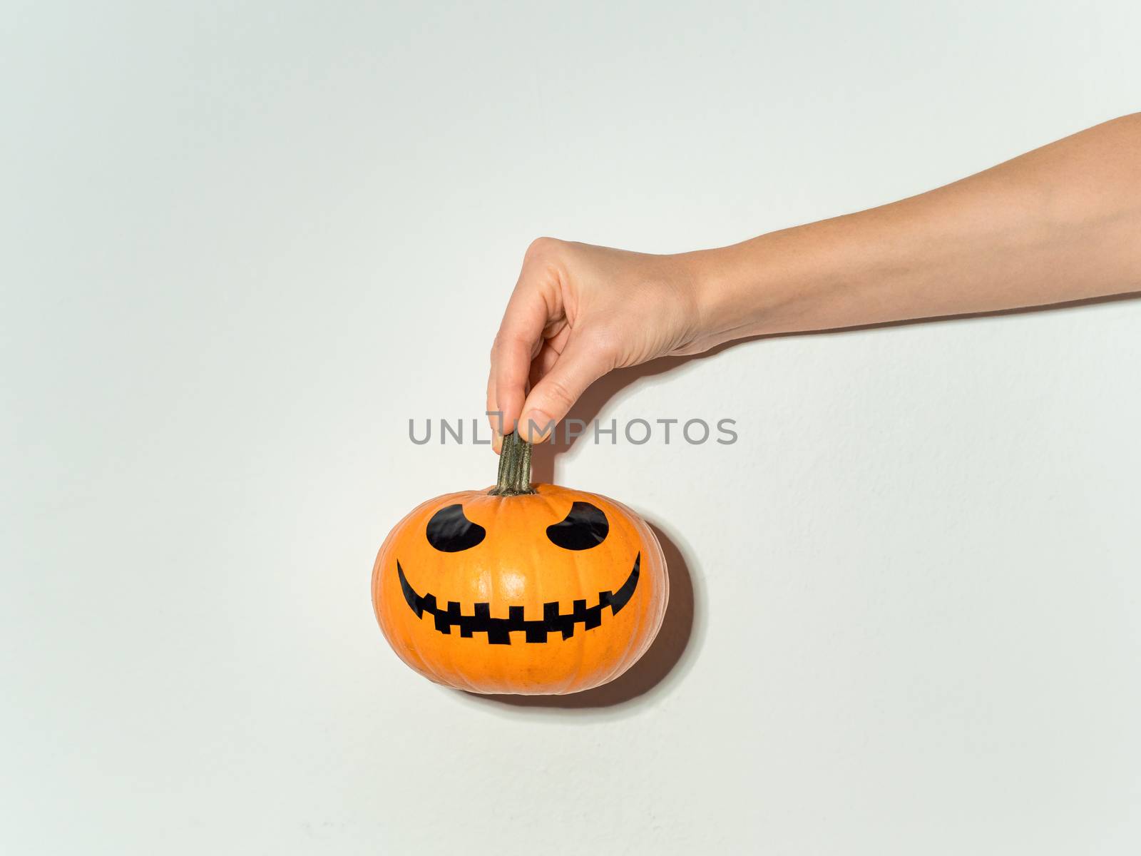 Hand holds halloween pumpkin on white wall by fascinadora