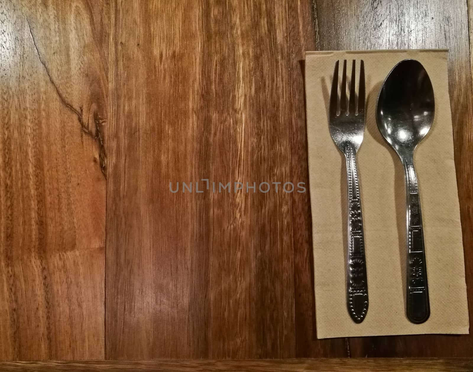 Silver spoon and fork on brown tissue paper on wooden table