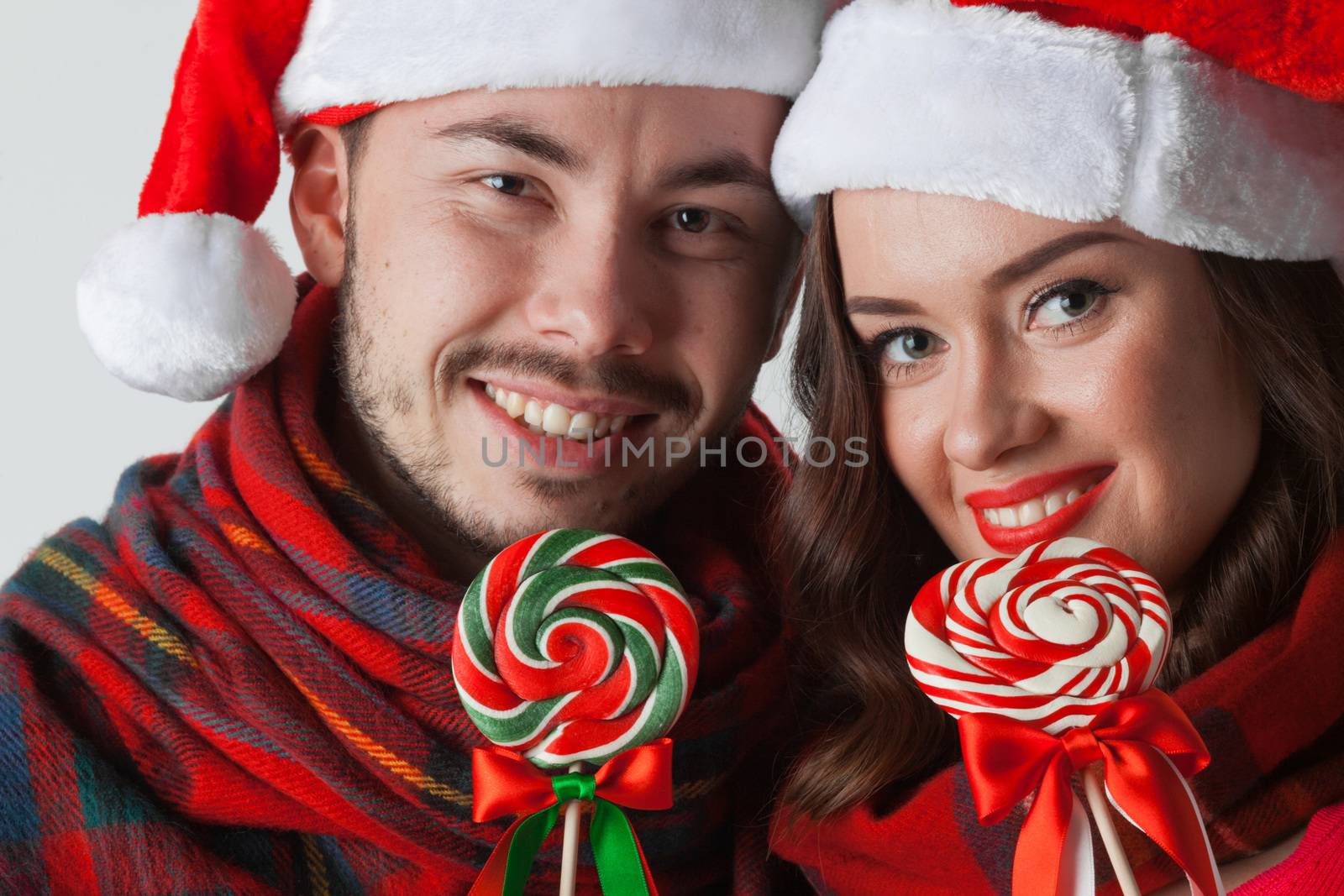 Young happy smiling couple in christmas santa hats with lollipops