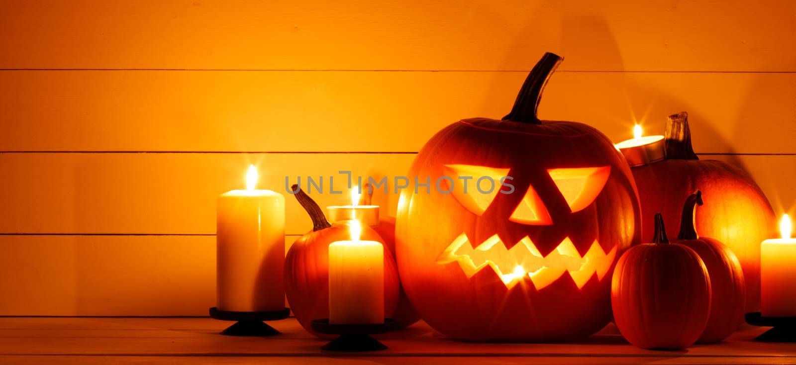 Halloween pumpkin head lantern and burning candles orange holiday background