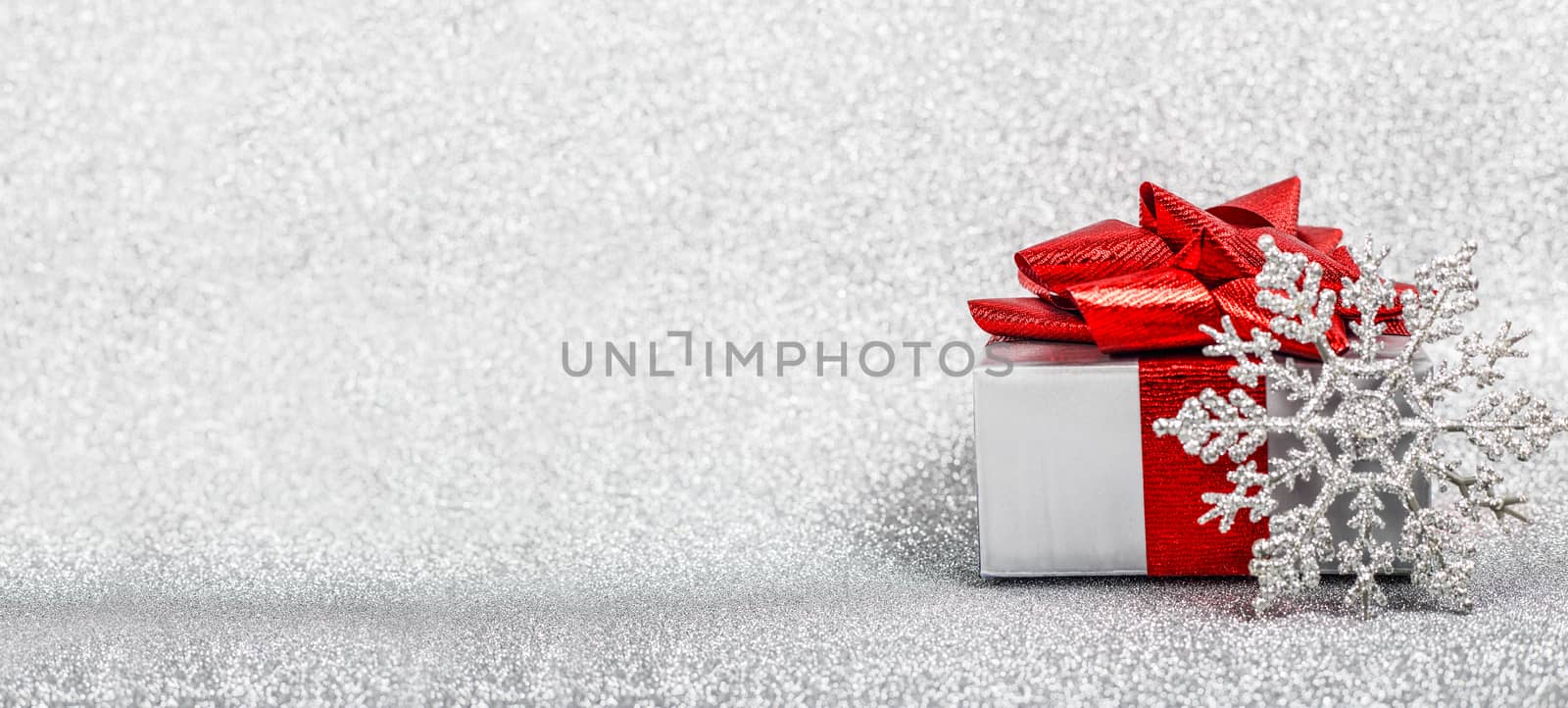 Christmas holiday composition of festive decor gift box with red ribbon on silver glitter bokeh background