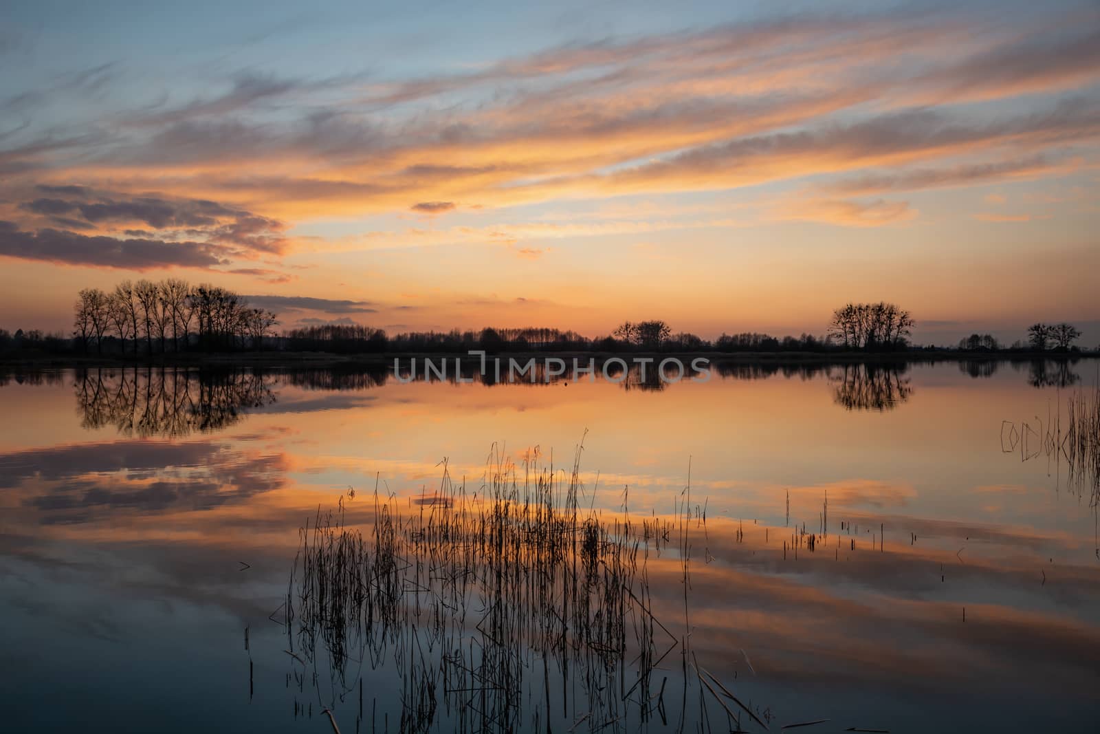 Reflection of clouds in the water after sunset, March evening at the lake