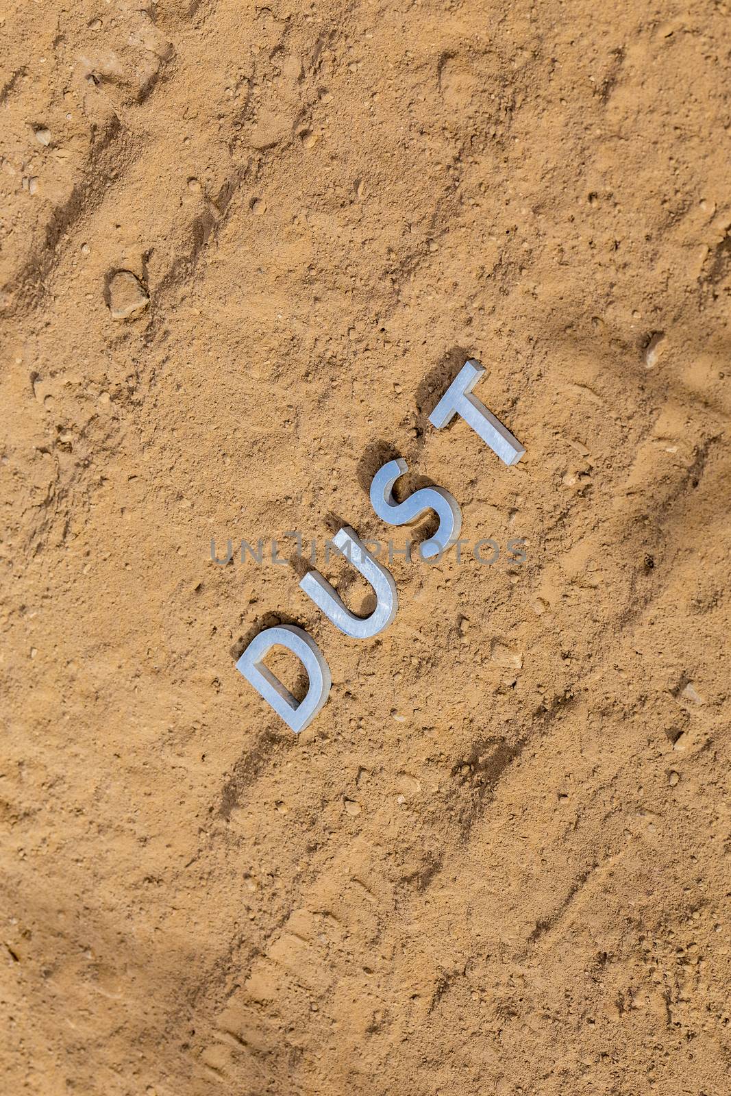 the word dust laid with silver metal letters on dusty road surface - close-up under direct sunlight