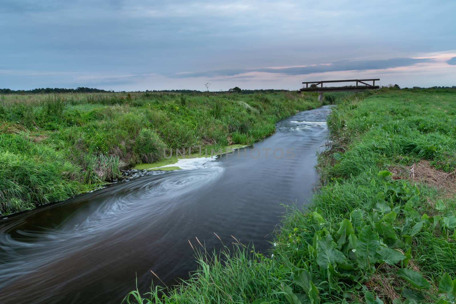 A river flowing through green wild meadows in eastern Poland, evening summer landscape