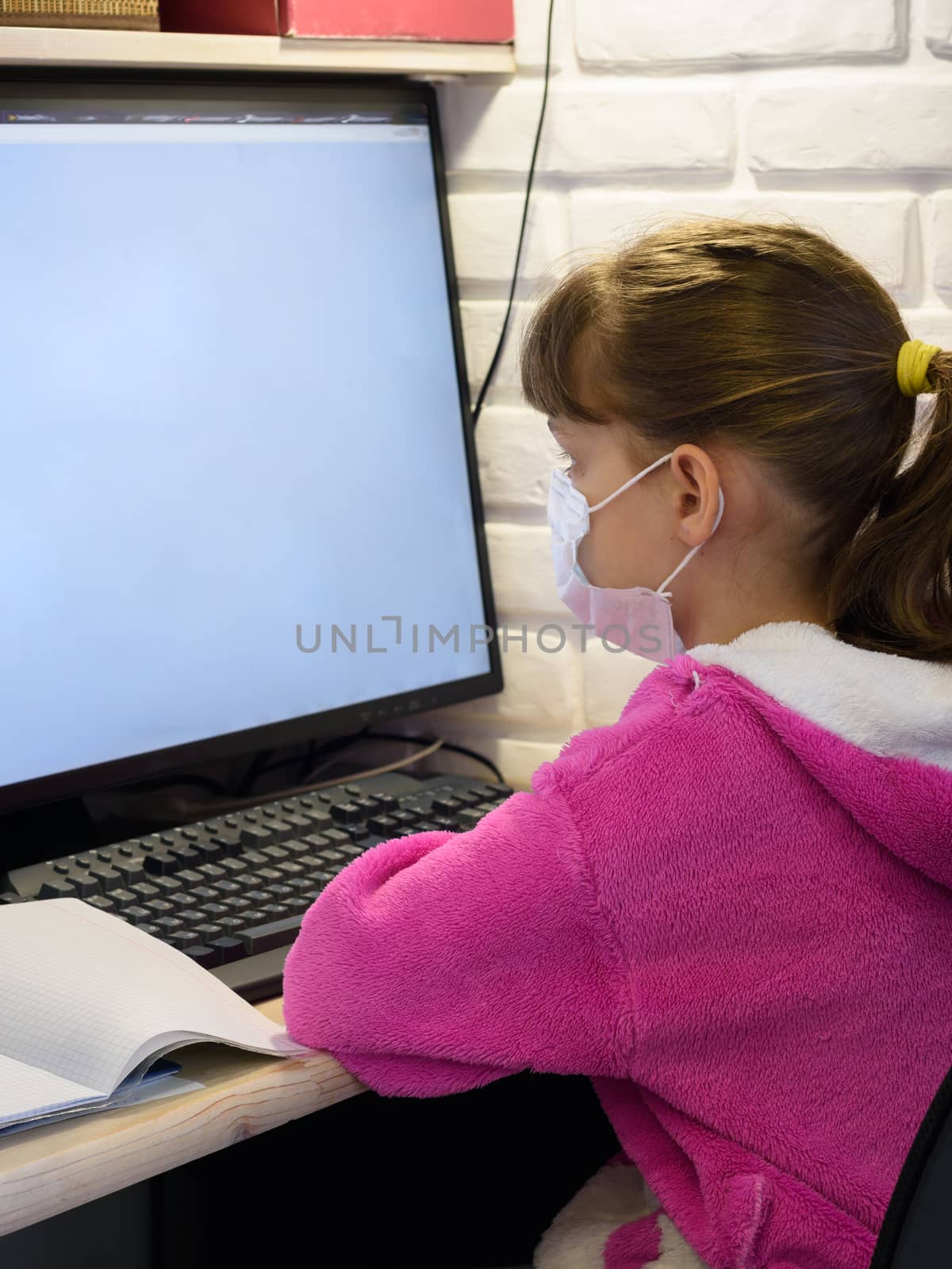 A girl in a medical mask sits at a computer and learns online by Madhourse