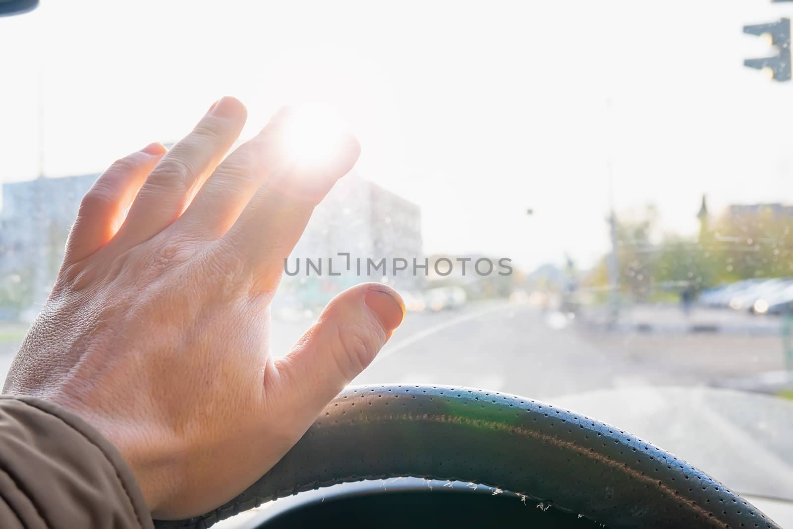 driver's hand at the wheel of the car covers the blinding sun by jk3030