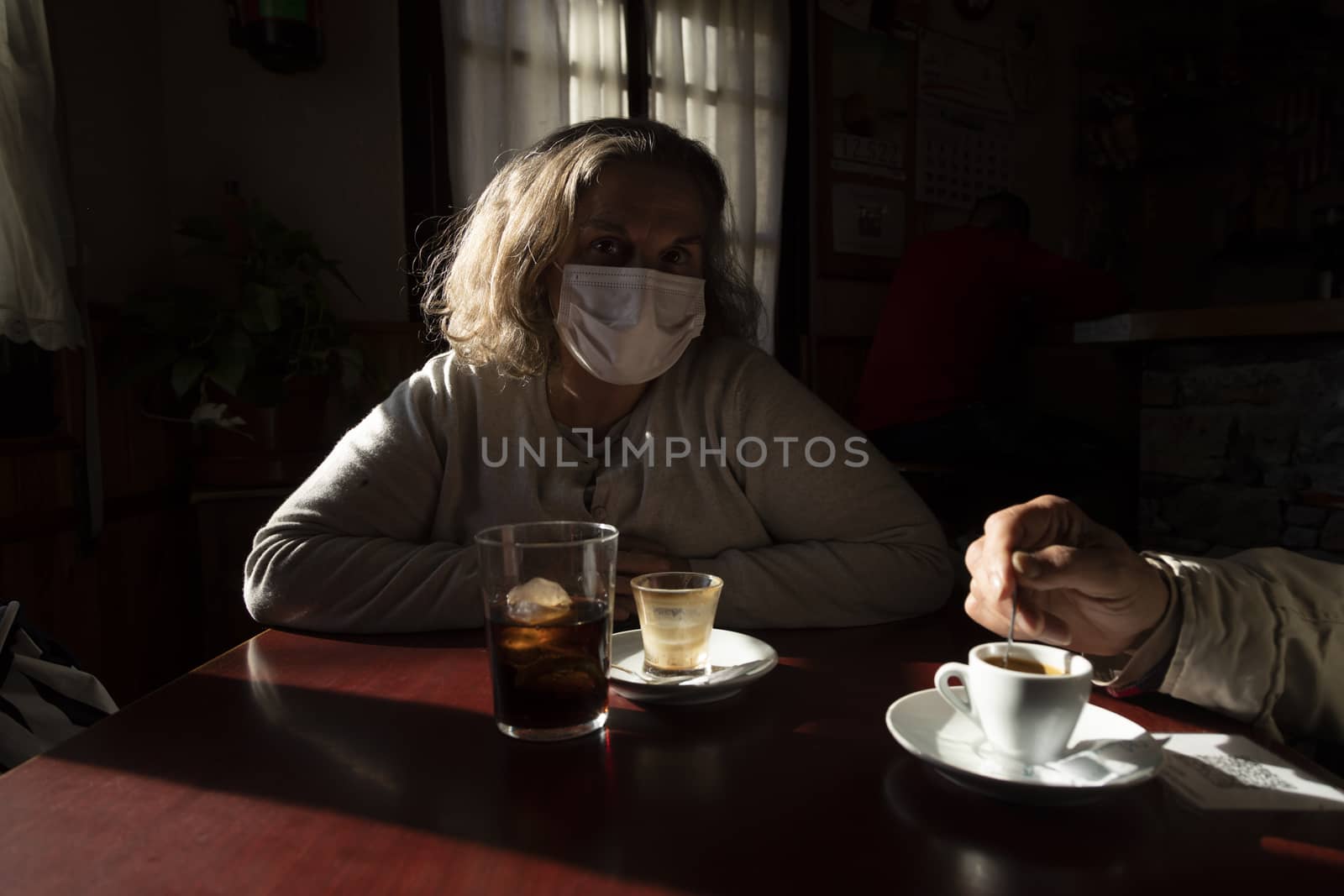 A woman, wearing a mask, watches sitting at a bar table, Spain by alvarobueno