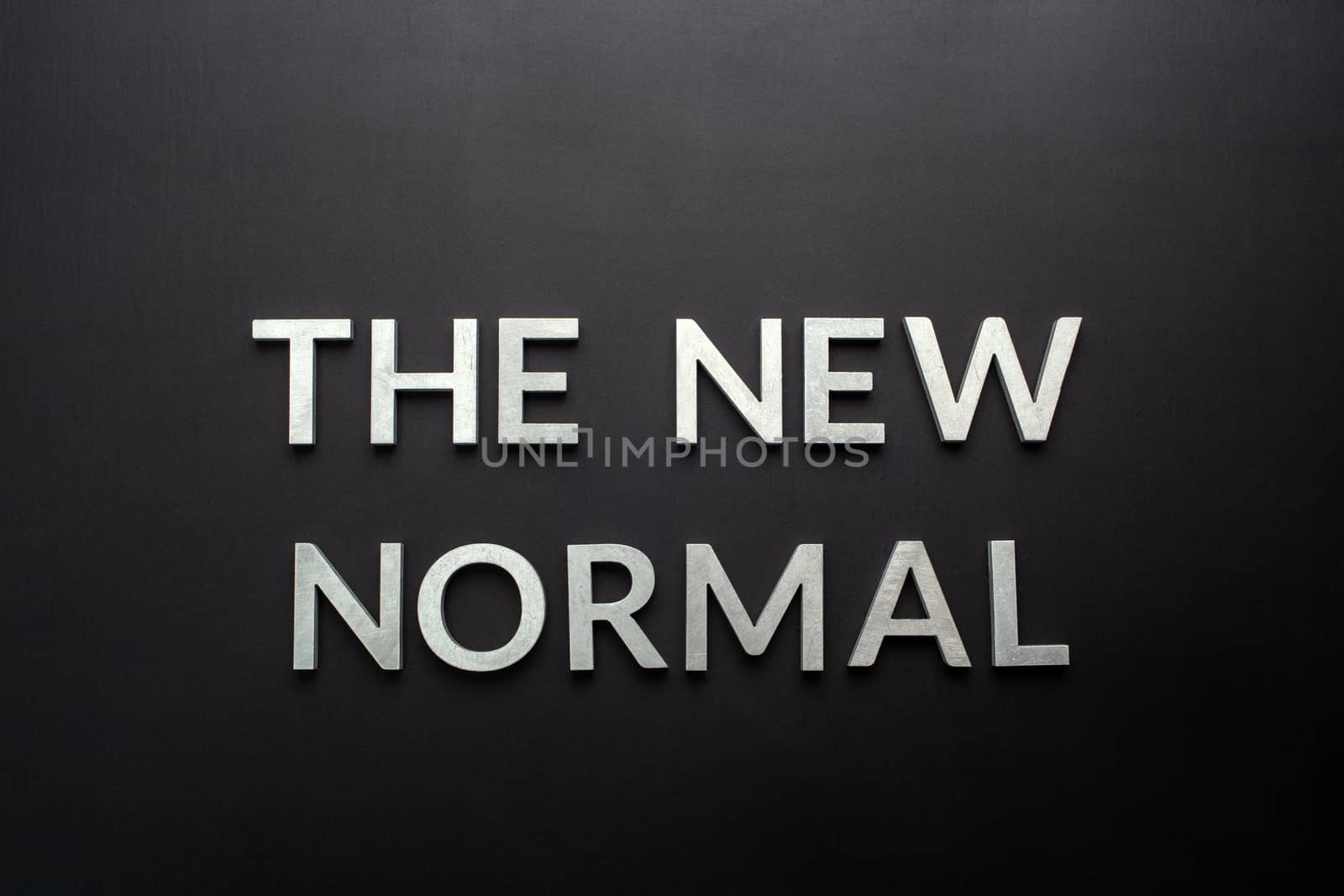 words the new normal laid with silver metal letters on flat black matte surface directly above in flat lay perspective.