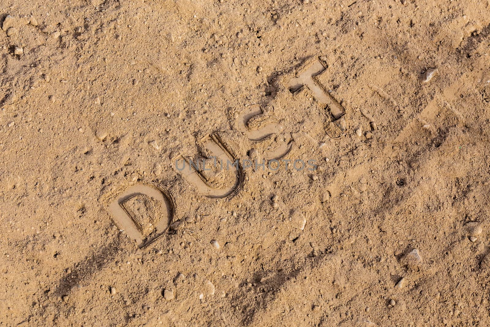 the word dust physically imprinted or embossed on dusty road surface - close-up flat lay perspective under direct sunlight