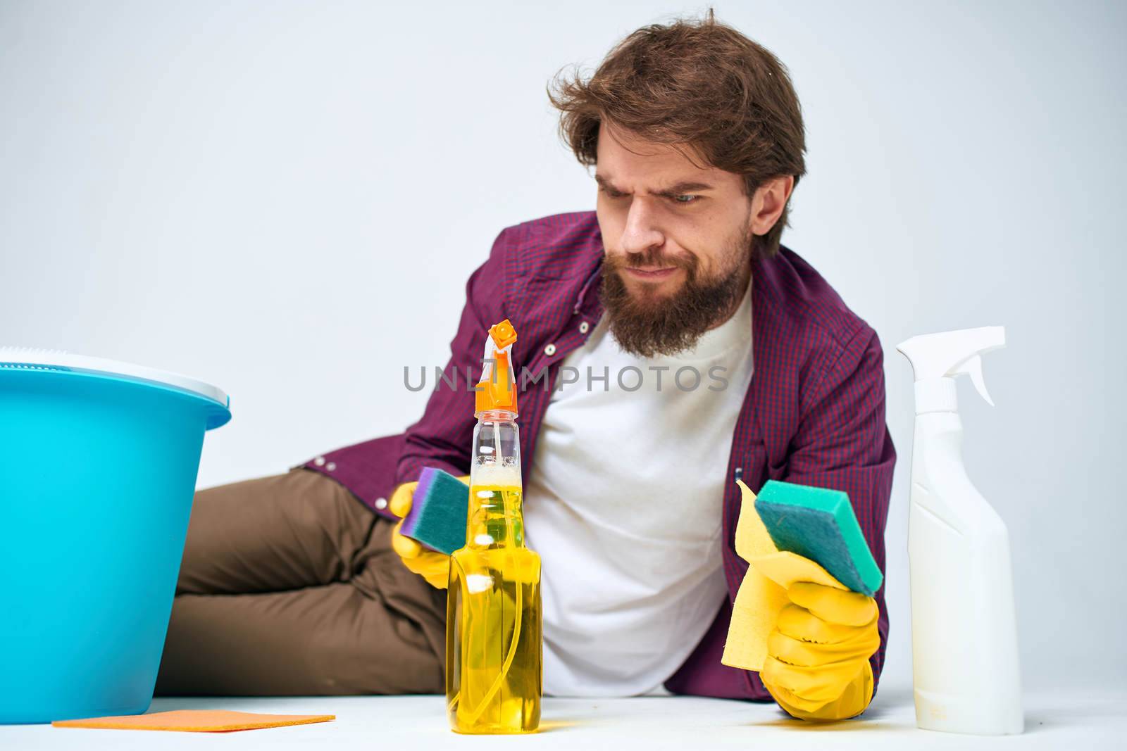 A man lies on the floor with a bucket of detergents providing services light background. High quality photo