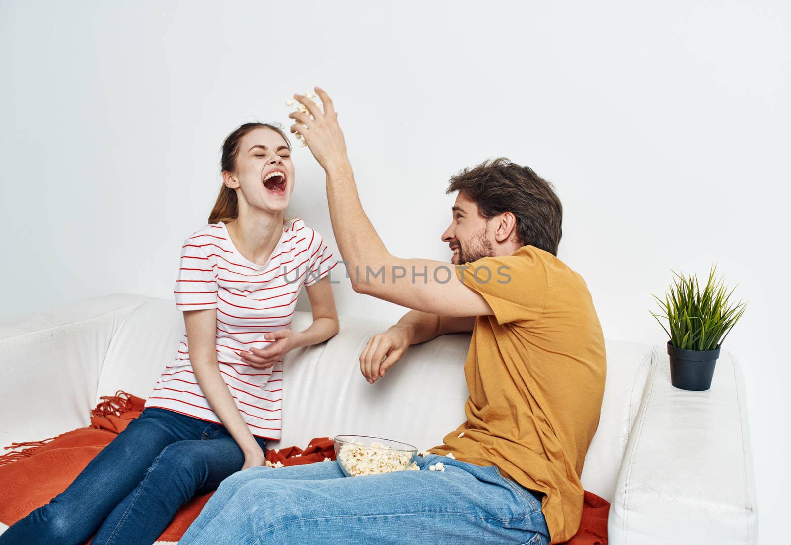 cheerful man and woman on the couch with popcorn and red plaid flower in a pot emotions. High quality photo