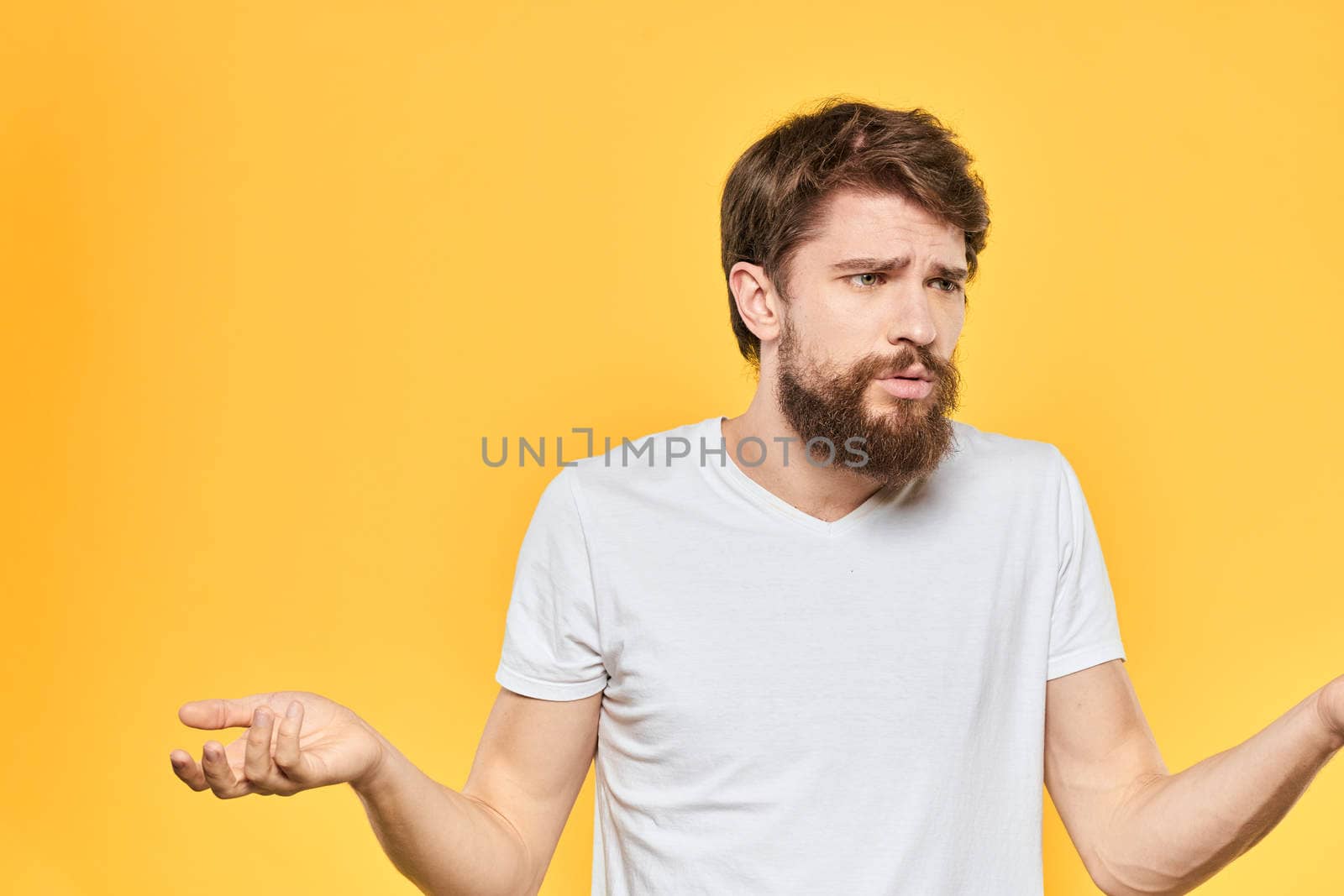 Bearded man in a white T-shirt gestures with his hands emotions studio yellow background. High quality photo