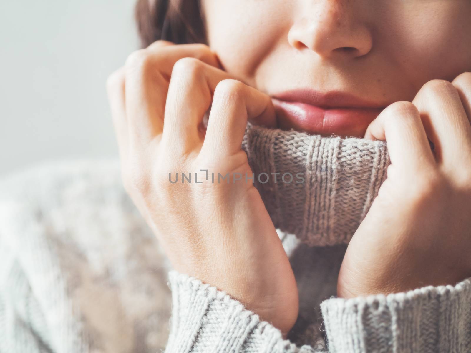 Close up portrait of woman snuggling in warm grey sweater. Casual outfit for cold weather at winter season.