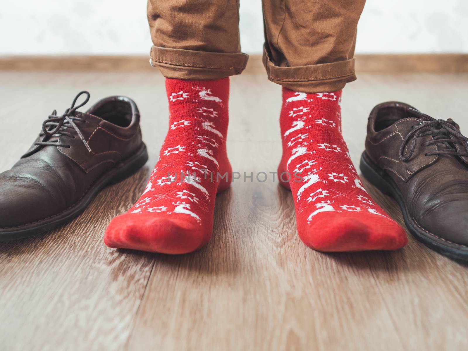 Young man in chinos trousers and bright red socks with reindeers on them is ready to wear sude shoes. Scandinavian pattern. Winter holiday spirit. Casual outfit for New Year and Christmas celebration.