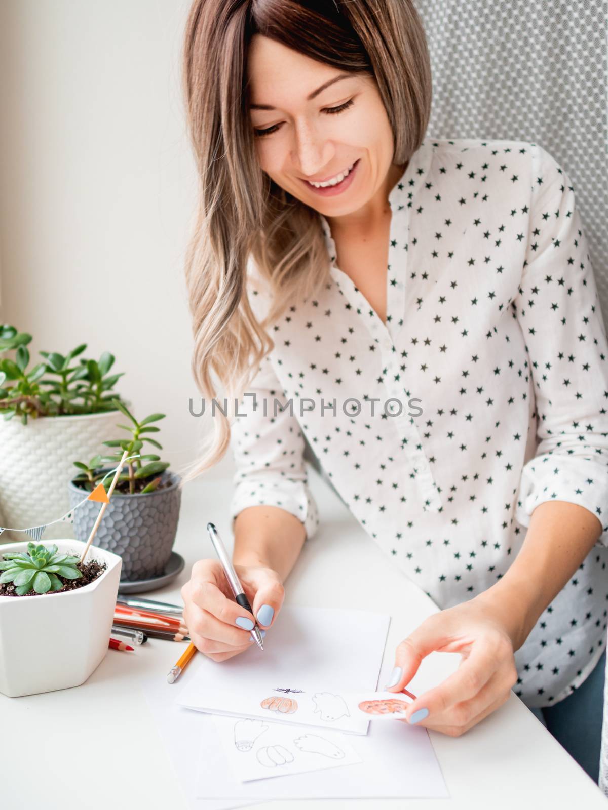 Woman decorates flower pots with handmade Halloween stickers. Hand drawn ghosts, flags and pumpkins in flower pot with succulent plant.