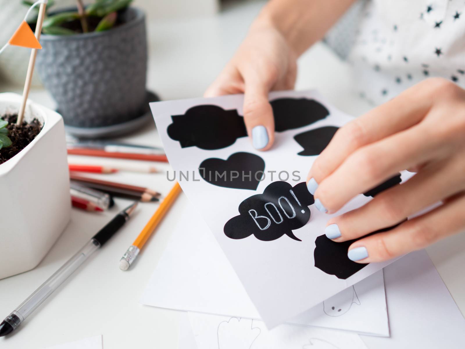 Woman writes Boo! on decorative black stickers for chalks. Handmade decorations for Halloween.