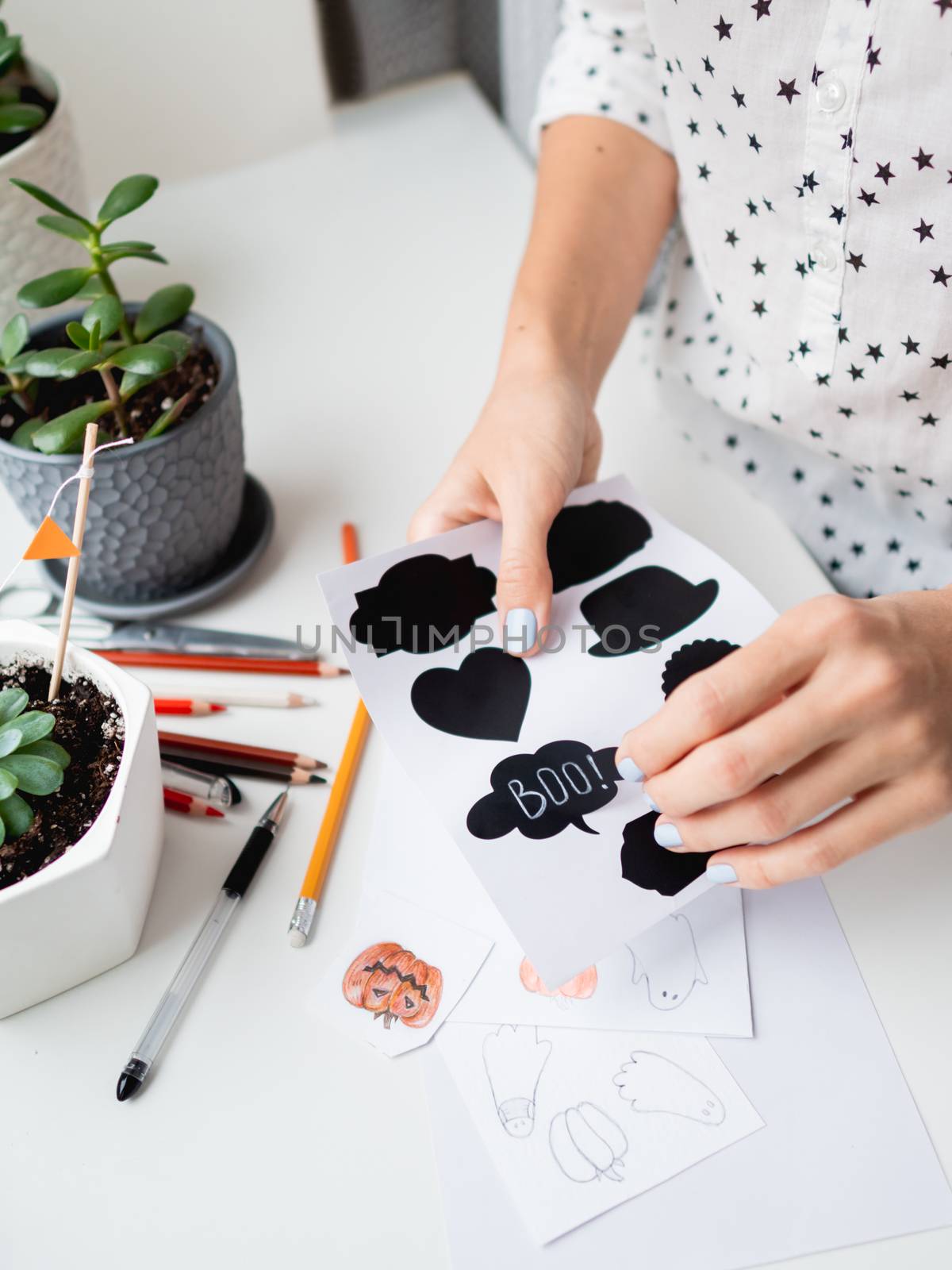 Woman writes Boo! on decorative black stickers for chalks. Handmade decorations for Halloween.
