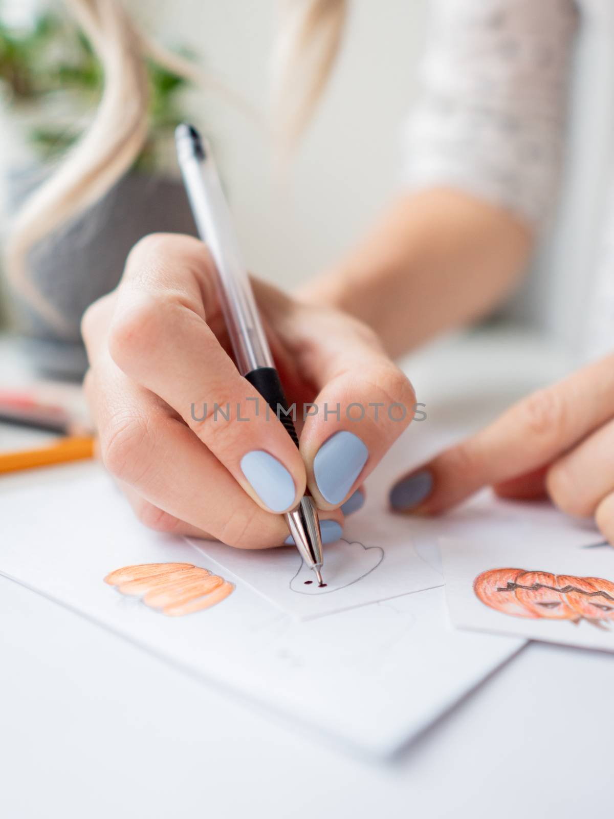 Woman with blue polish on nails draw ghosts and pumpkins. Handma by aksenovko