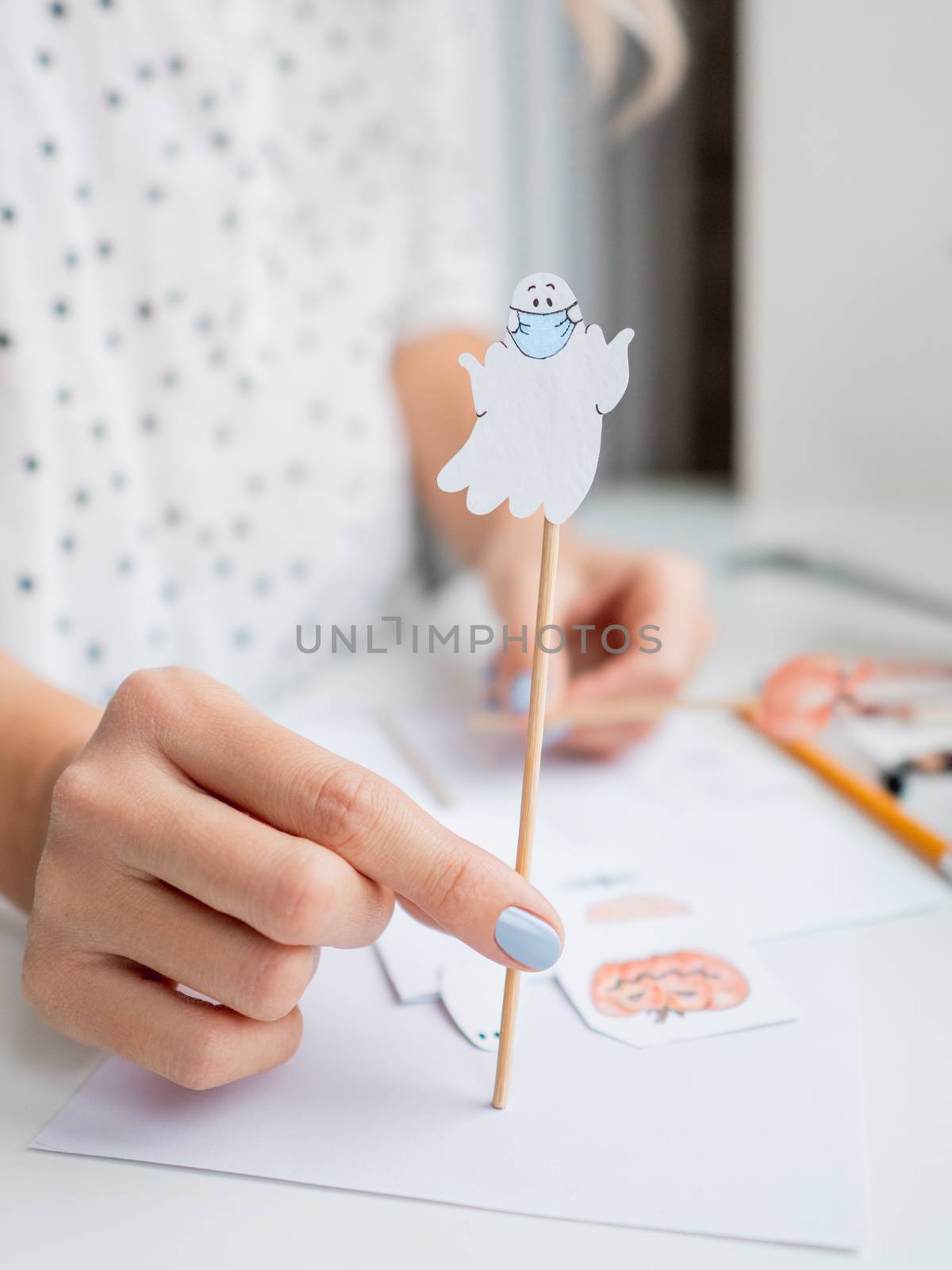 Woman with blue polish on nails paints ghost in medical protecti by aksenovko