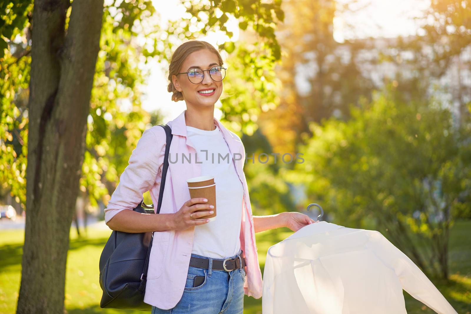 Businesswoman clothes designer standing summer park Business person Outdoors Successful european caucasian woman walking outside with black backpack dressed denim jeans white shirt pink jacket