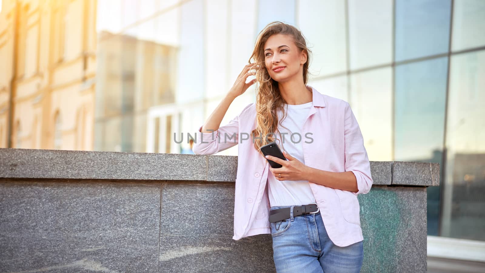 Businesswoman standing summer day near corporate building using smartphone teeth smiling Business person Outdoors Successful european caucasian woman freelancer dressed white shirt pink jacket