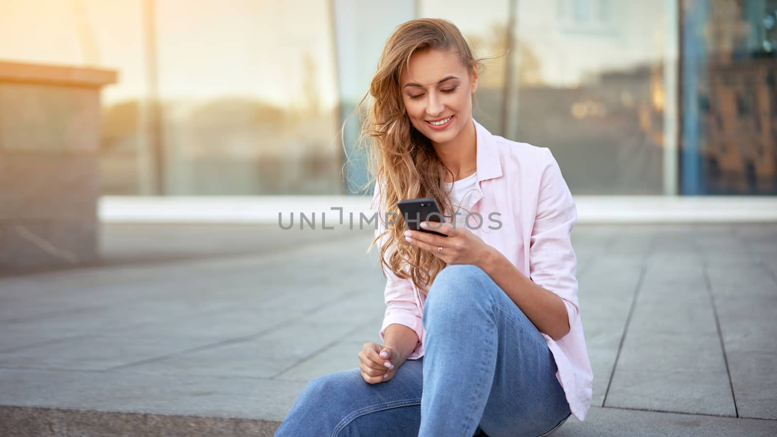 Businesswoman sitting summer day near corporate building using smartphone teeth smiling Business person Outdoors Successful european caucasian woman freelancer dressed white shirt pink jacket